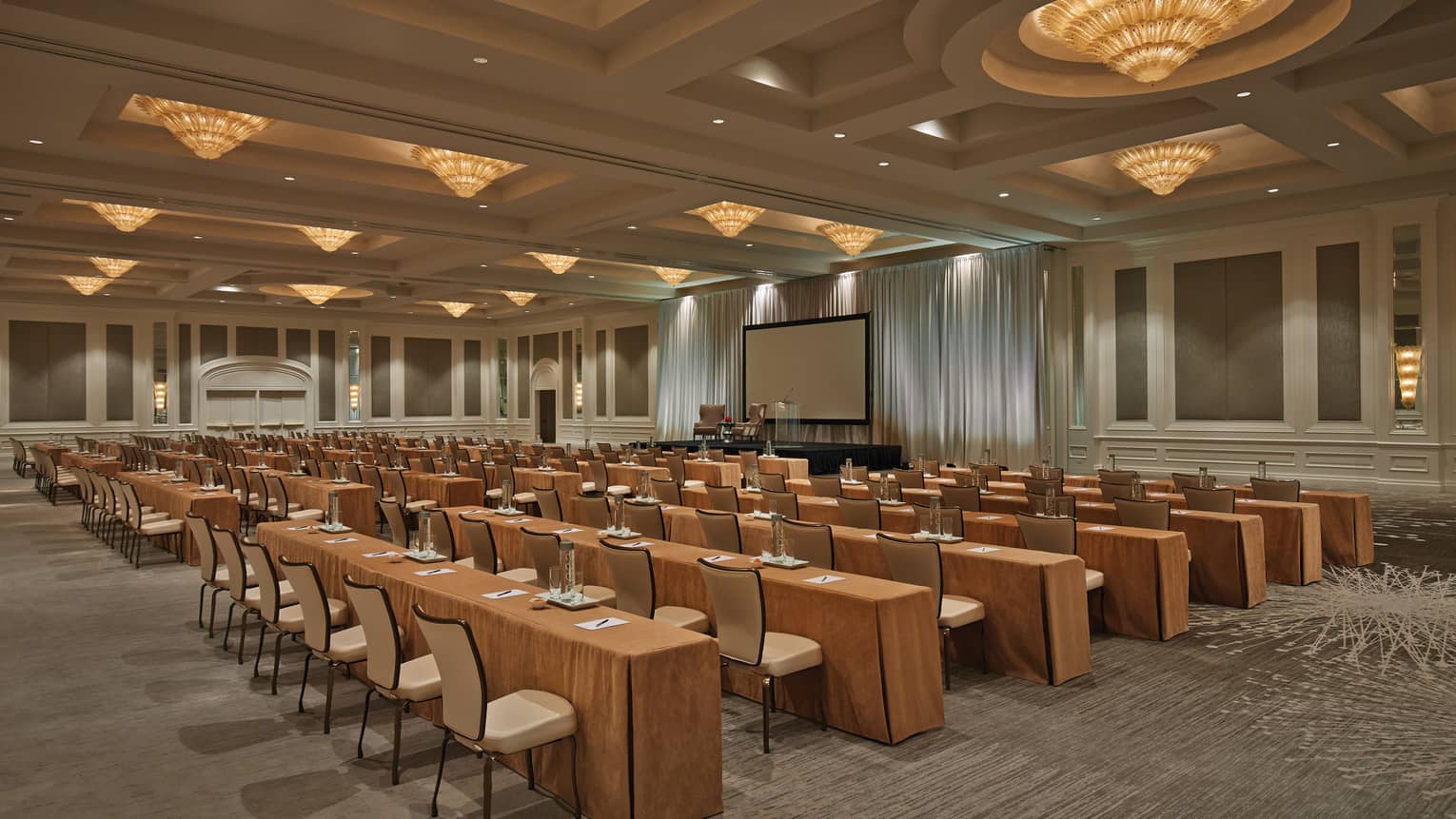 Conference with rows of meeting tables, chairs under cone-shaped lights in large ballroom