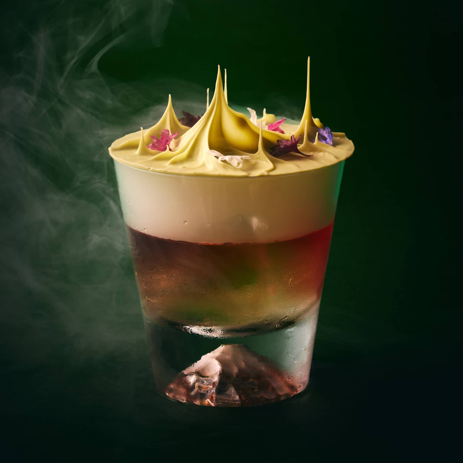 Cocktail topped with foam, floral garnishes and dry ice