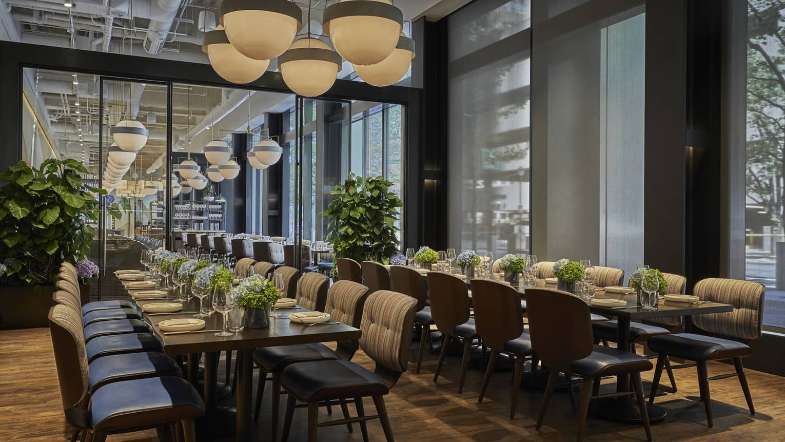 Two long tables are set with plates and white floral arrangements in Vernick Restaurant in Four Seasons Philadelphia