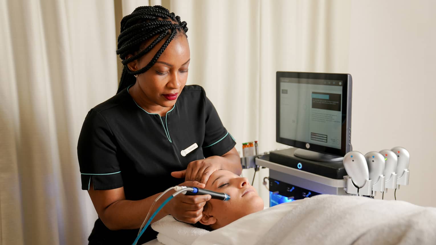 Spa technician places a scanning device on the face of a guest who is lying beneath a light-grey blanket