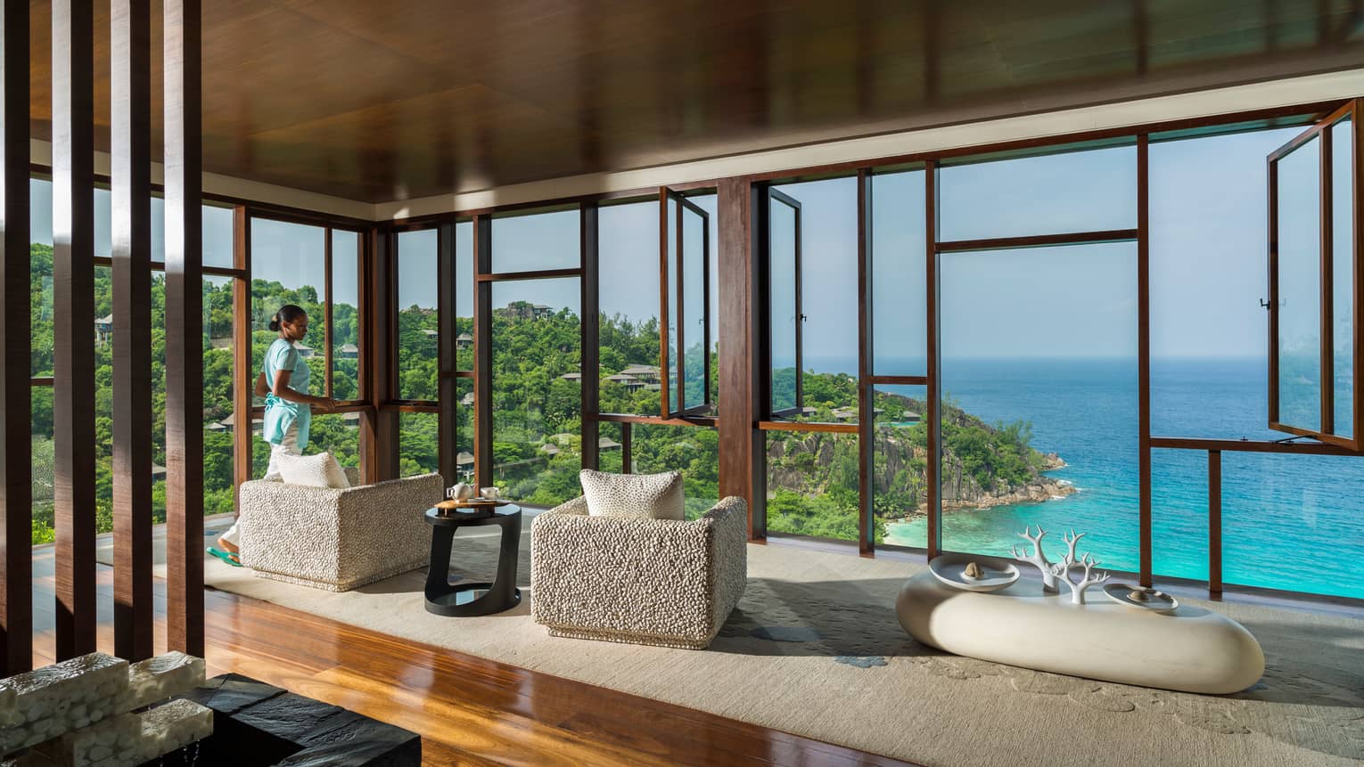 Spa relaxation centre under open-air beam roof with stone armchairs overlooking ocean, lush cliffs