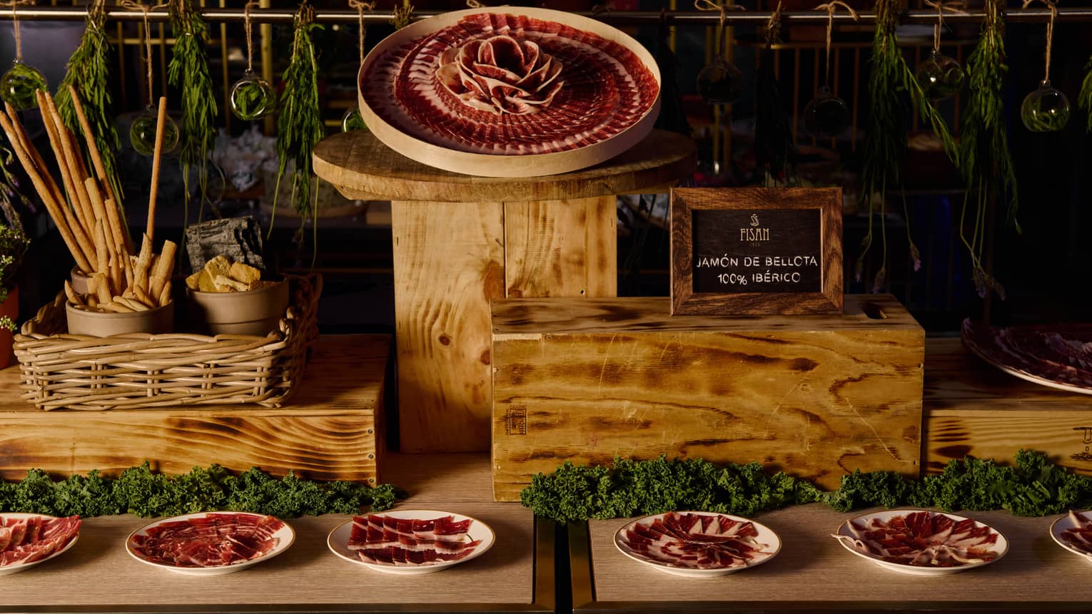 Tables holding wood stands displaying plates of sliced Iberian ham, plus other food items and decorative greenery