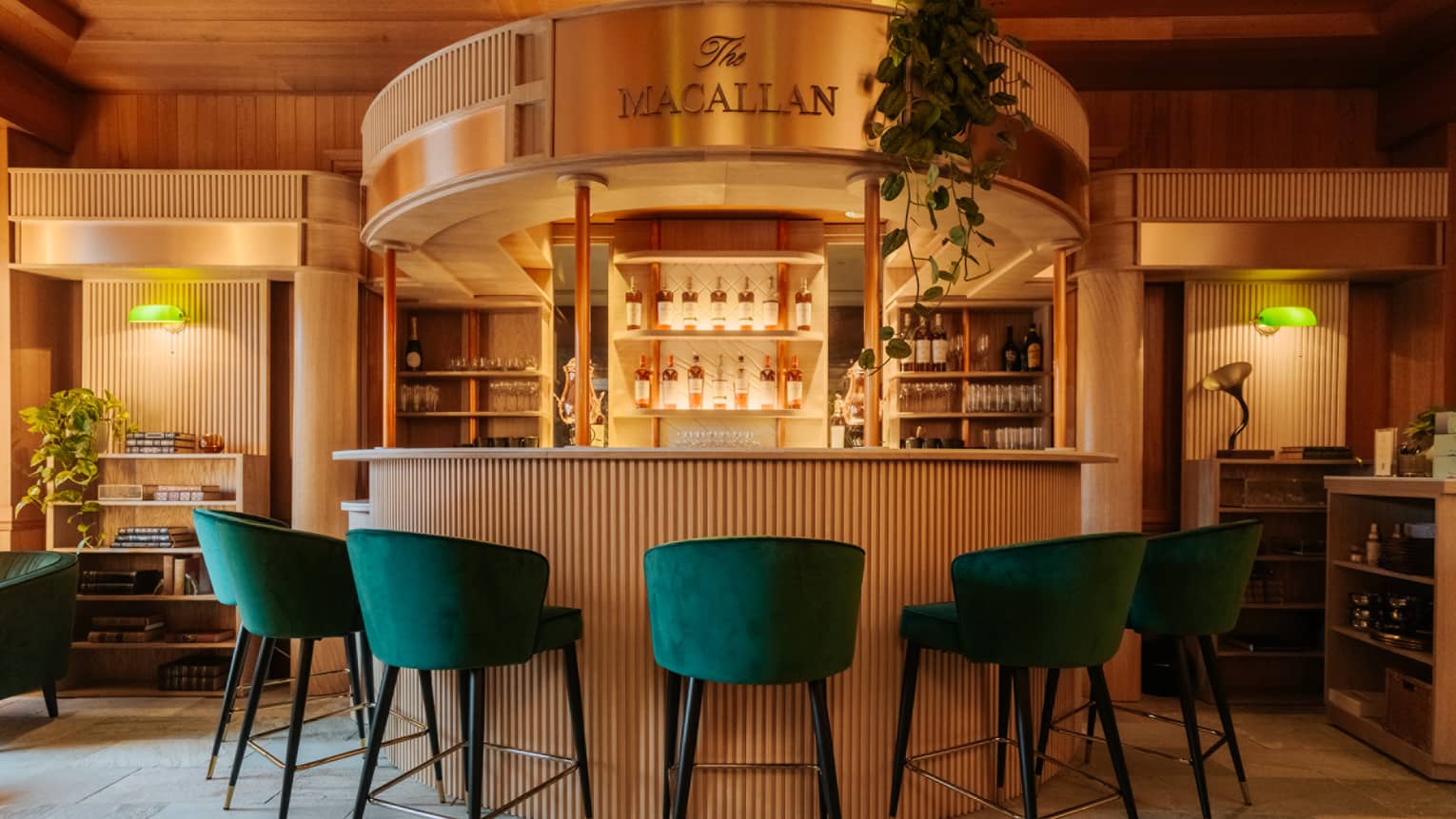 Half moon–shaped bar with green velvet bar stools and display of liquor bottles in background