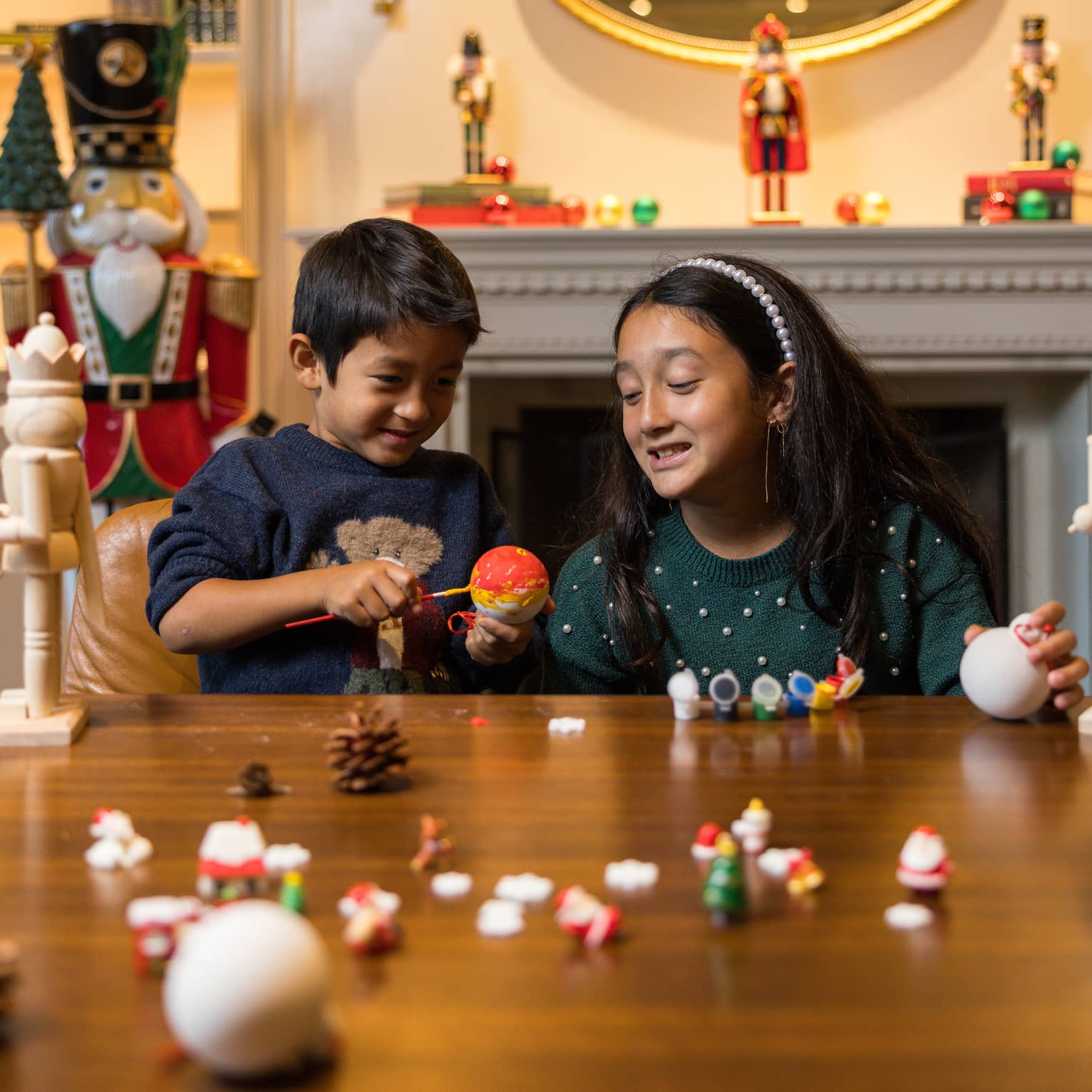 Two children sit at a table making Christmas ornaments