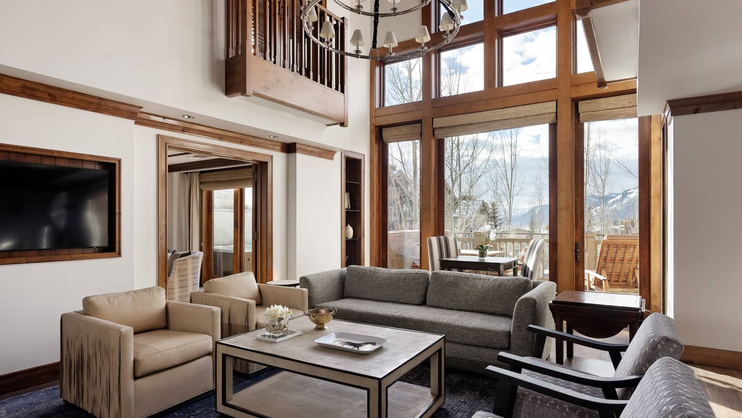 Living room with high ceilings, beige and grey patterned armchairs, grey sofa, coffee table and outdoor balcony with mountain view