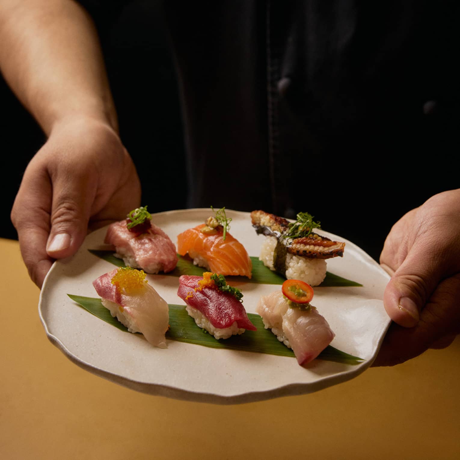 A person in a black shirt holds a plate with six different pieces of sushi.