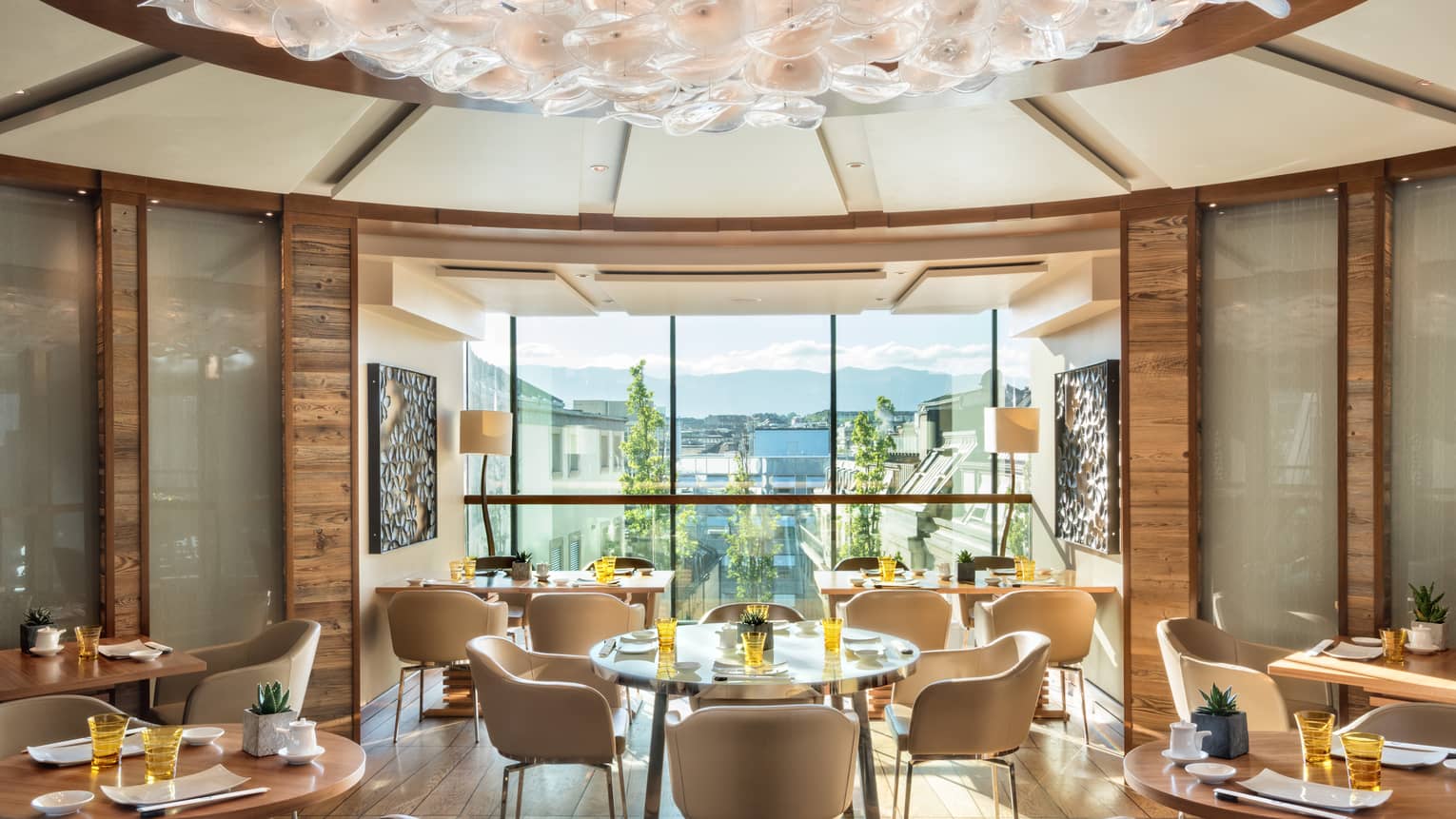Sunny rotunda dining room with cream-coloured chairs, round wood tables, floor-to-ceiling window