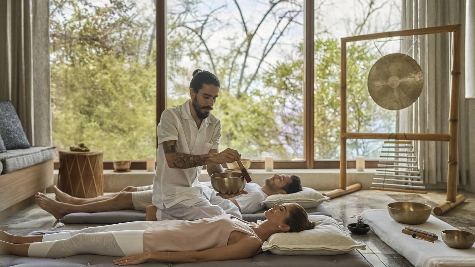 Two people on the floor in the Resort's Sound Room, as a man plays a Tibetan Singing Bowl next to them