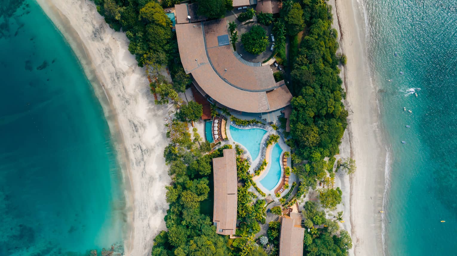 Aerial view of pool and buildings on a strip of green land bookended by water on either side