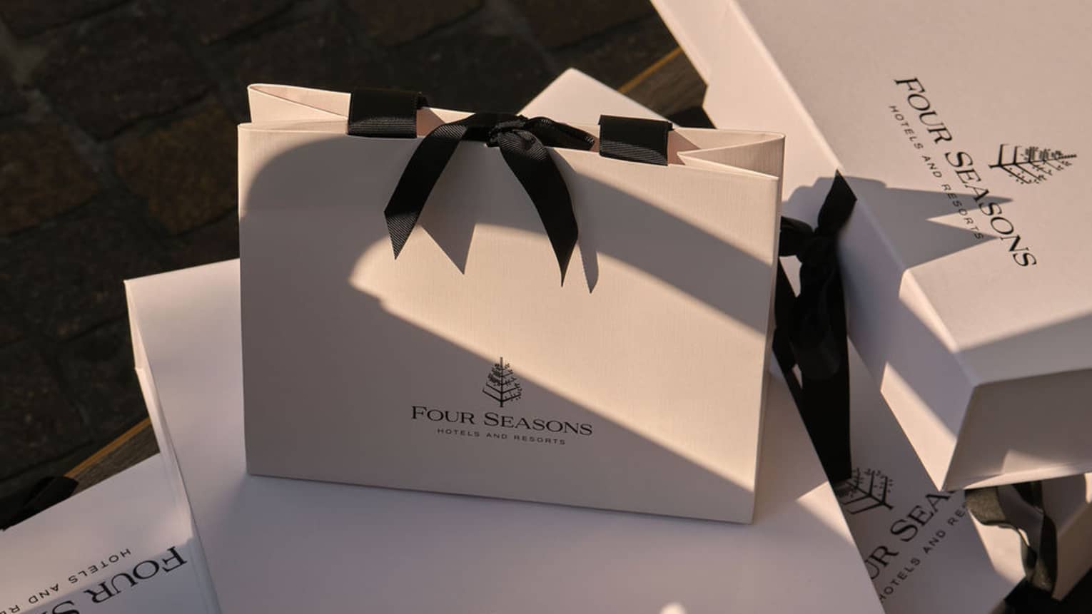White gift boxes and bags with black bows and the Four Seasons logo