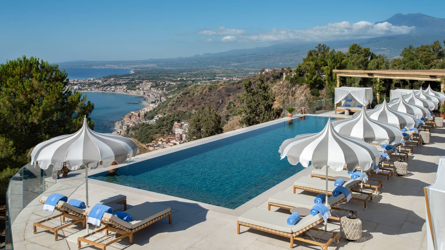Rectangular pool, lounge chairs and umbrellas overlooking sea and Mount Etna
