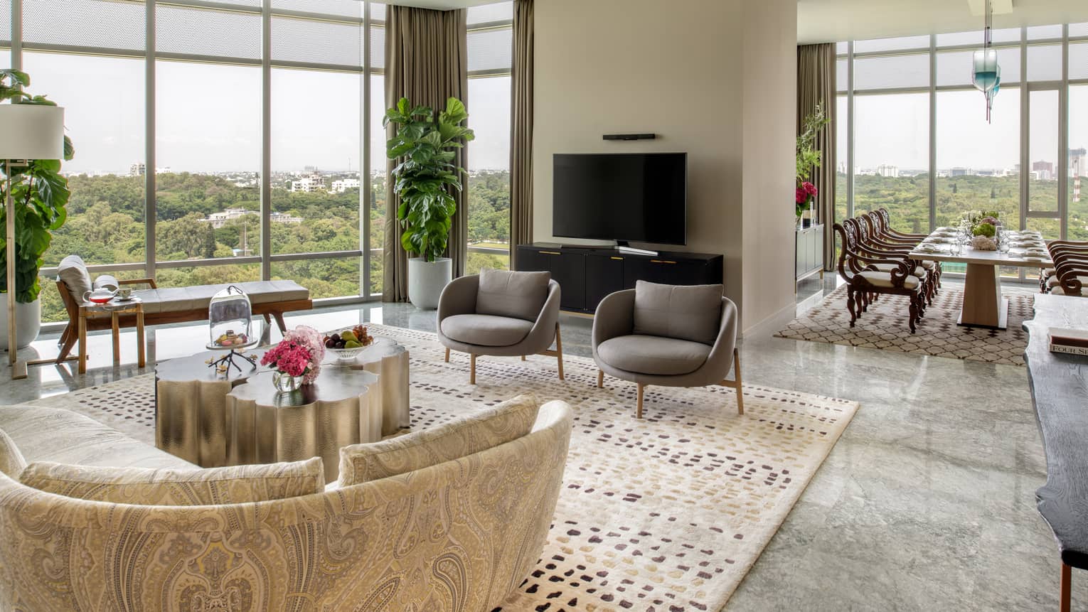 Guest room living area with patterned sectional sofa, grey armchairs, floor-to-ceiling windows, doorway to dining area with long rectangular table