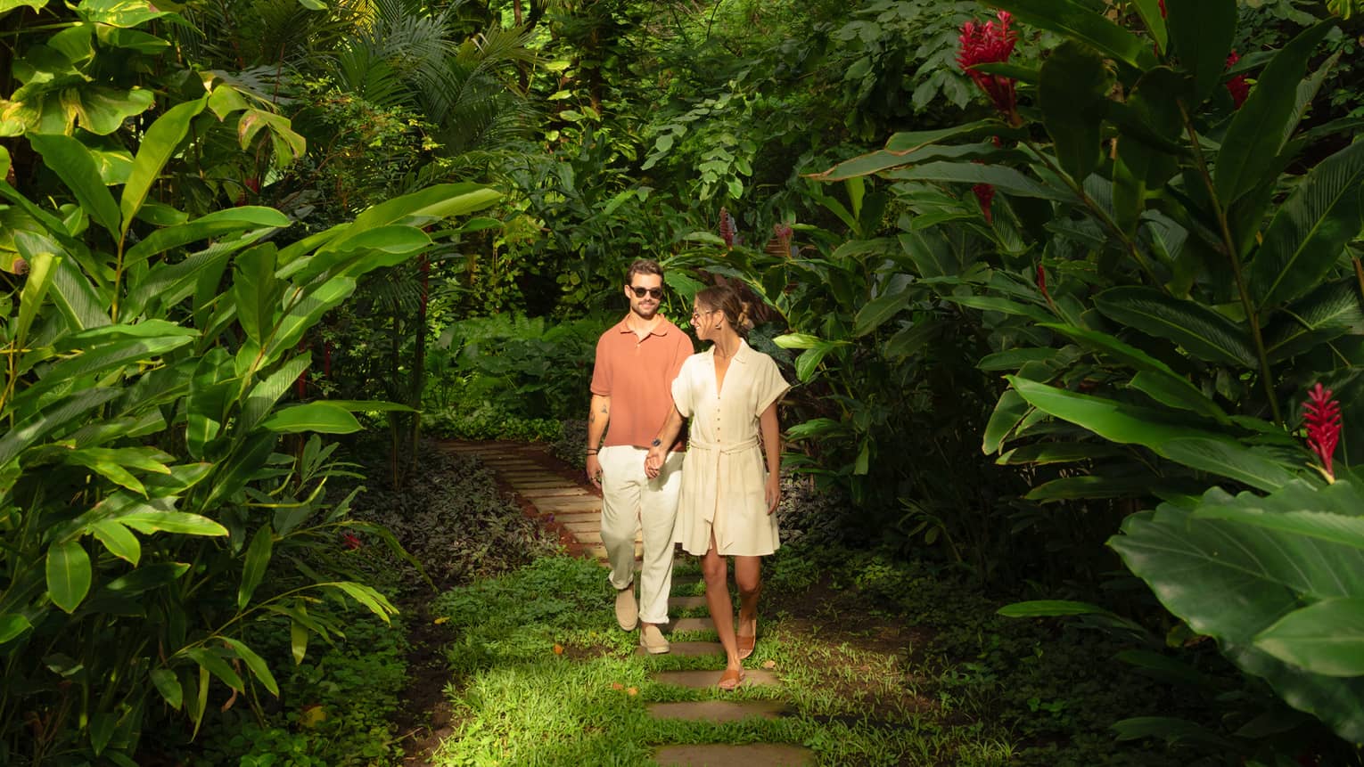 A couple walks hand-in-hand through a tropical jungle