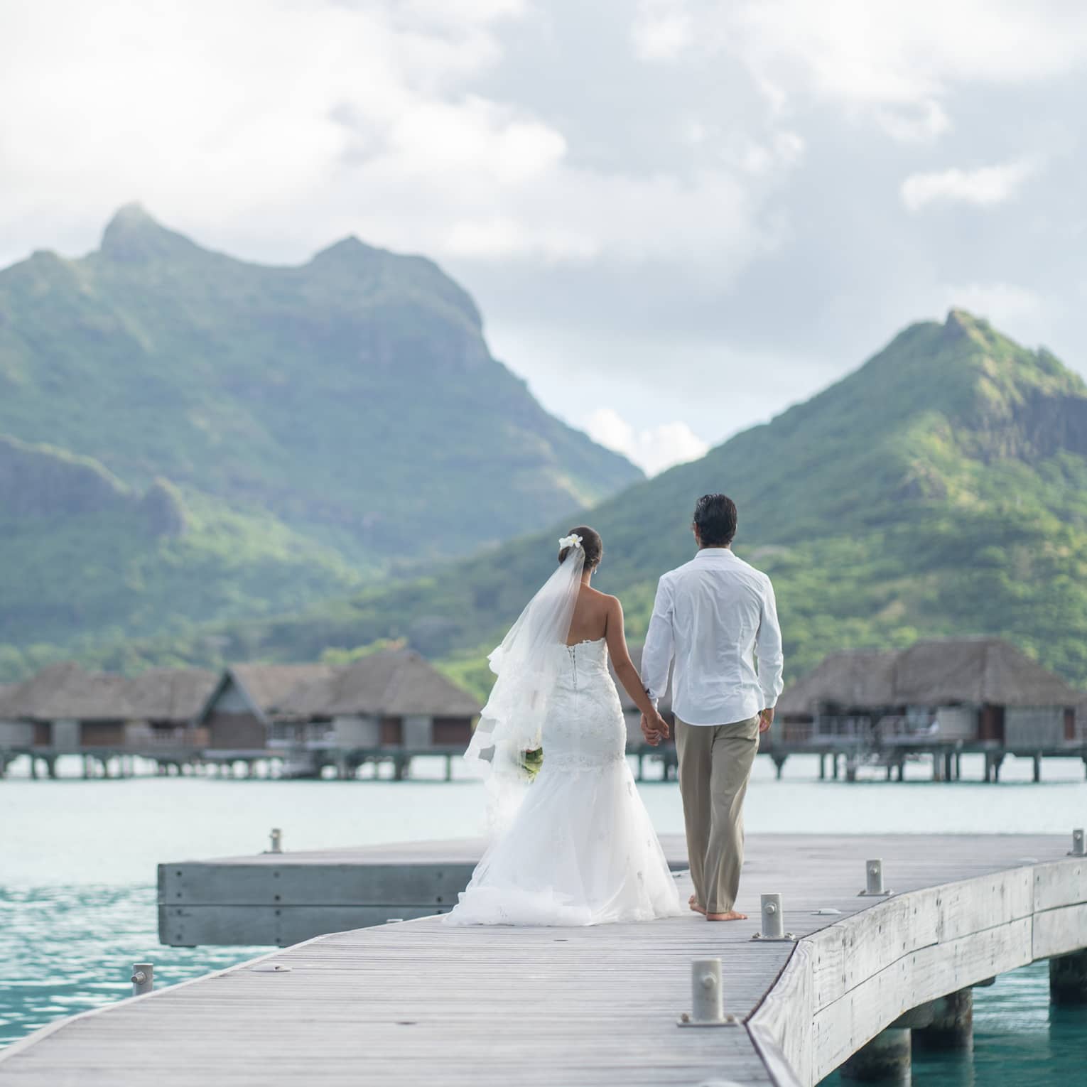 Bride and groom on overwater bungalow walkway, Bora Bora mountains in background