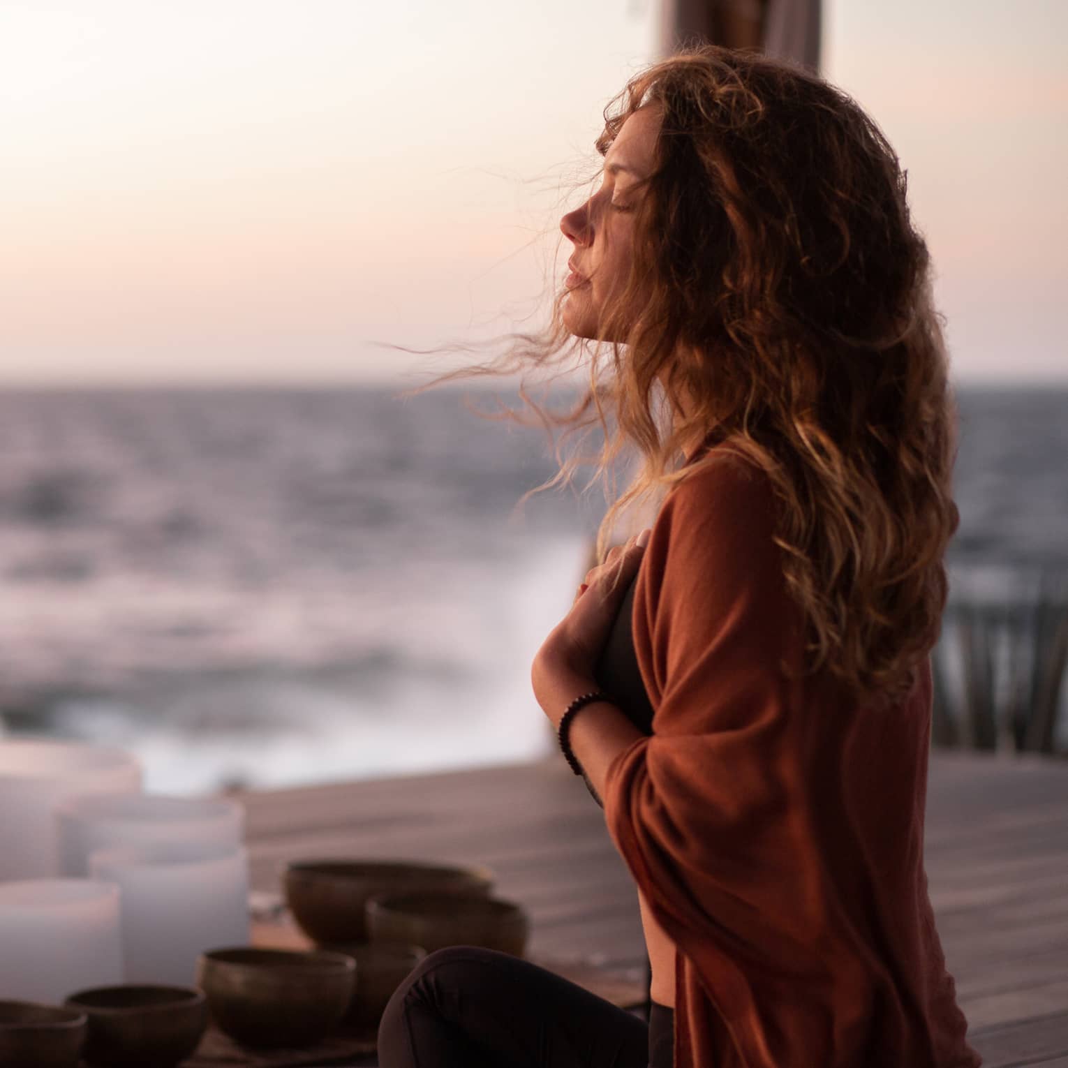 A woman participating in breathwork and sound meditation outside near an ocean.