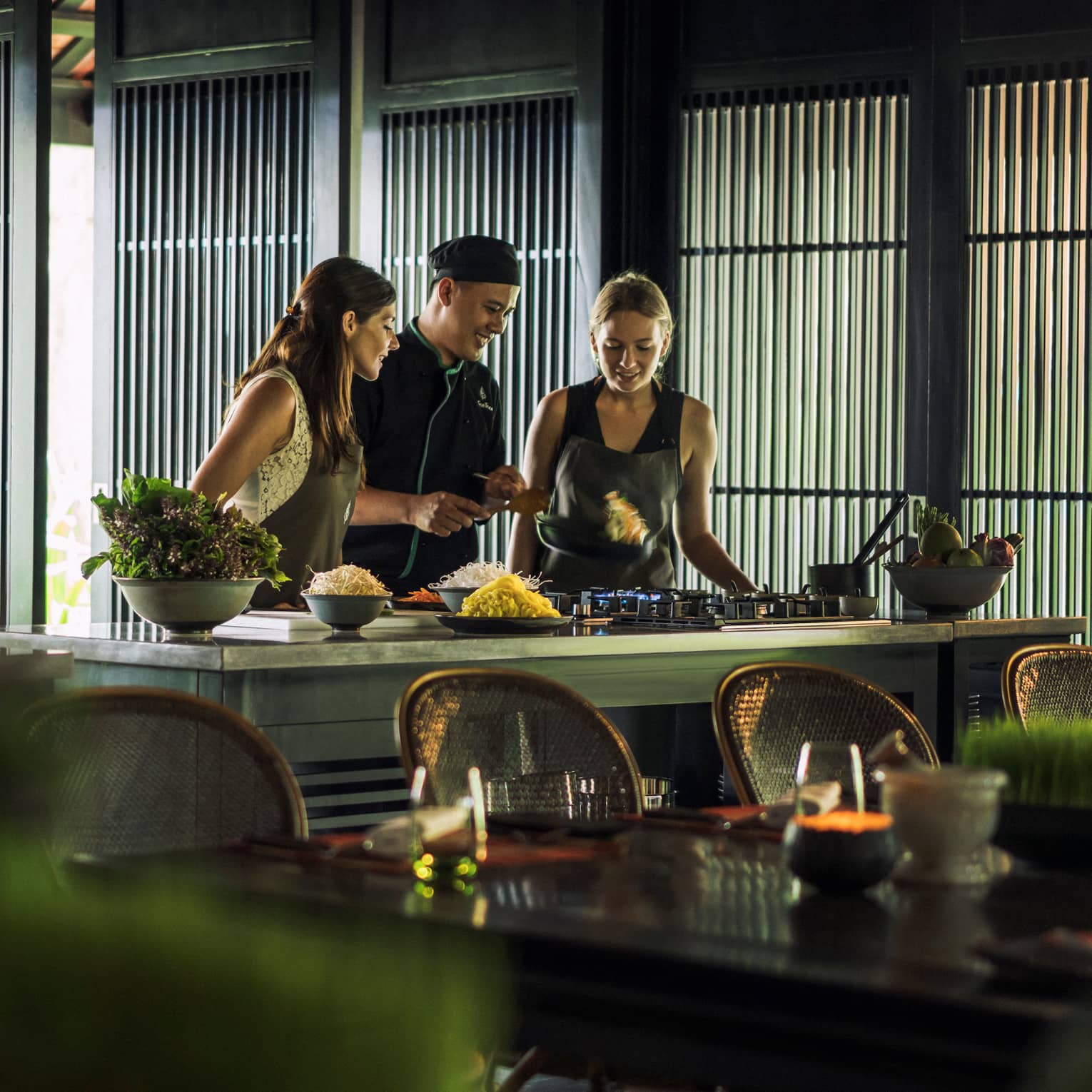 Chef, two women look at pan on kitchen range at Hoi An Cooking Academy