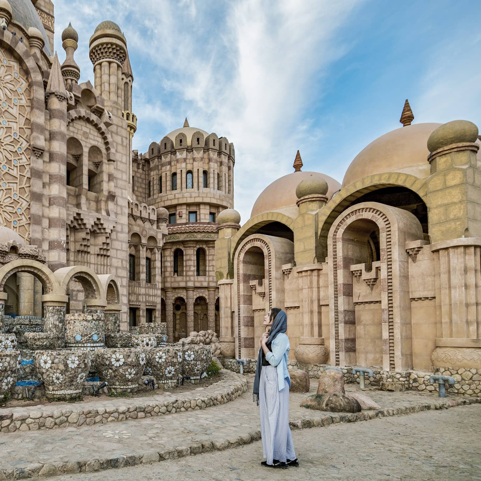 A guest stands in front of a large, intricately tiled stone building, gazing at its numerous turrets, archways and domes.