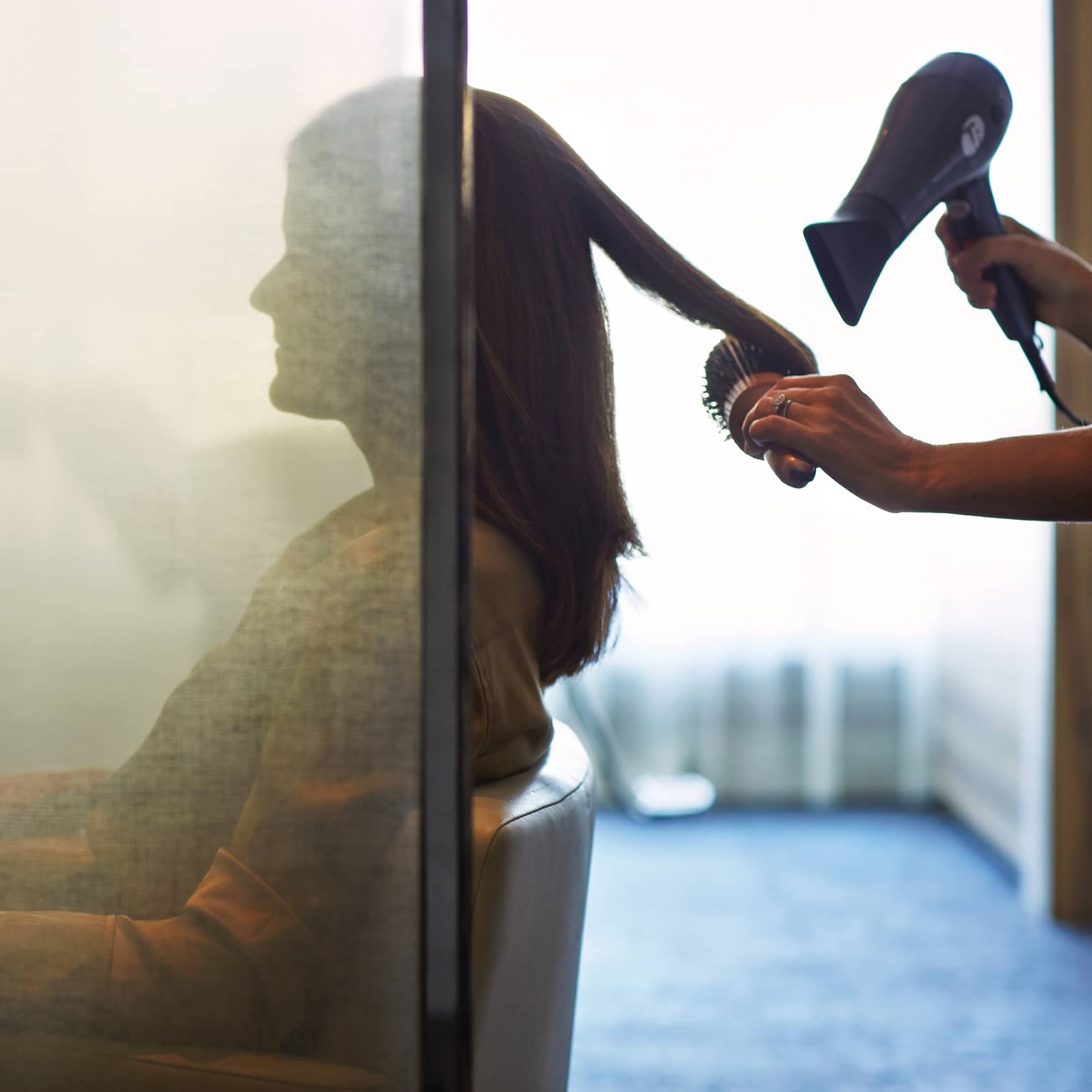 Silhouette of woman behind salon screen as hairdressers brushes, blow dries hair