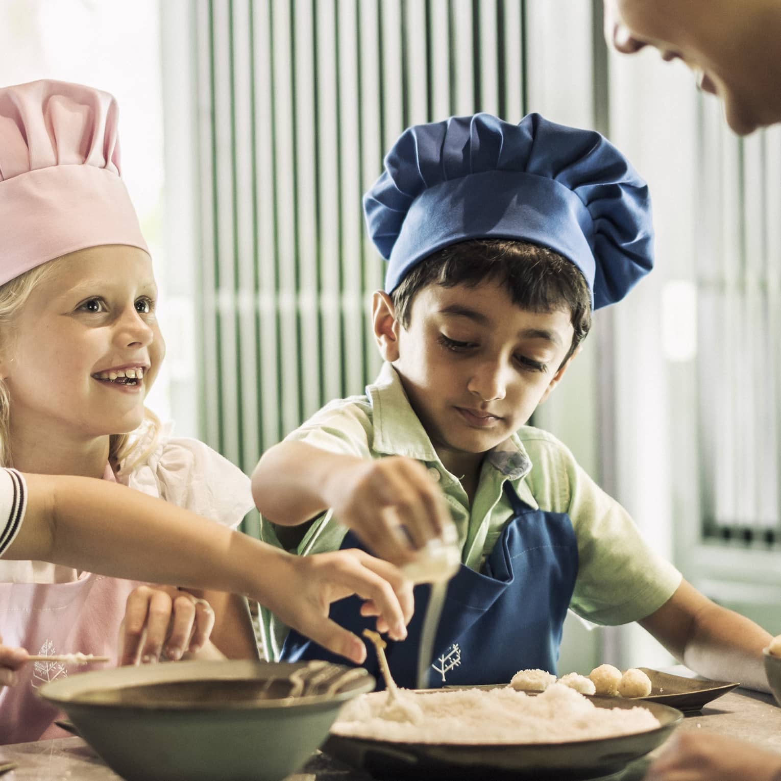 Three children with pink or blue chefs hats making food.