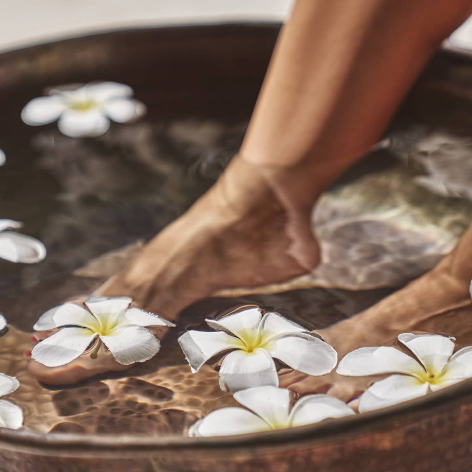 A woman's feet in a bowl of water and flowers.