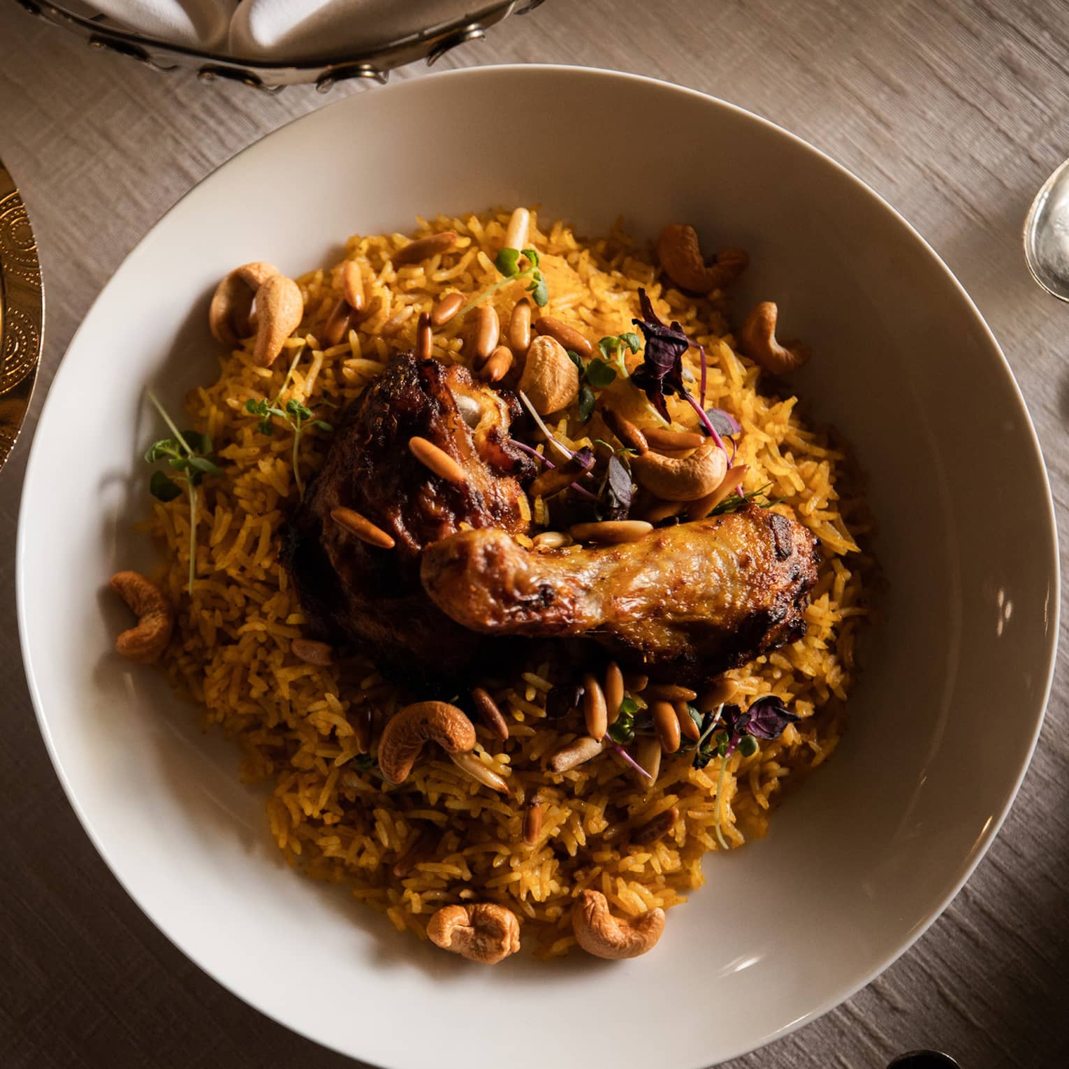 A view from above bowl of Kabsa, an Arabic chicken and rice dish, beautifully arranged with silver dishes surrounding it.