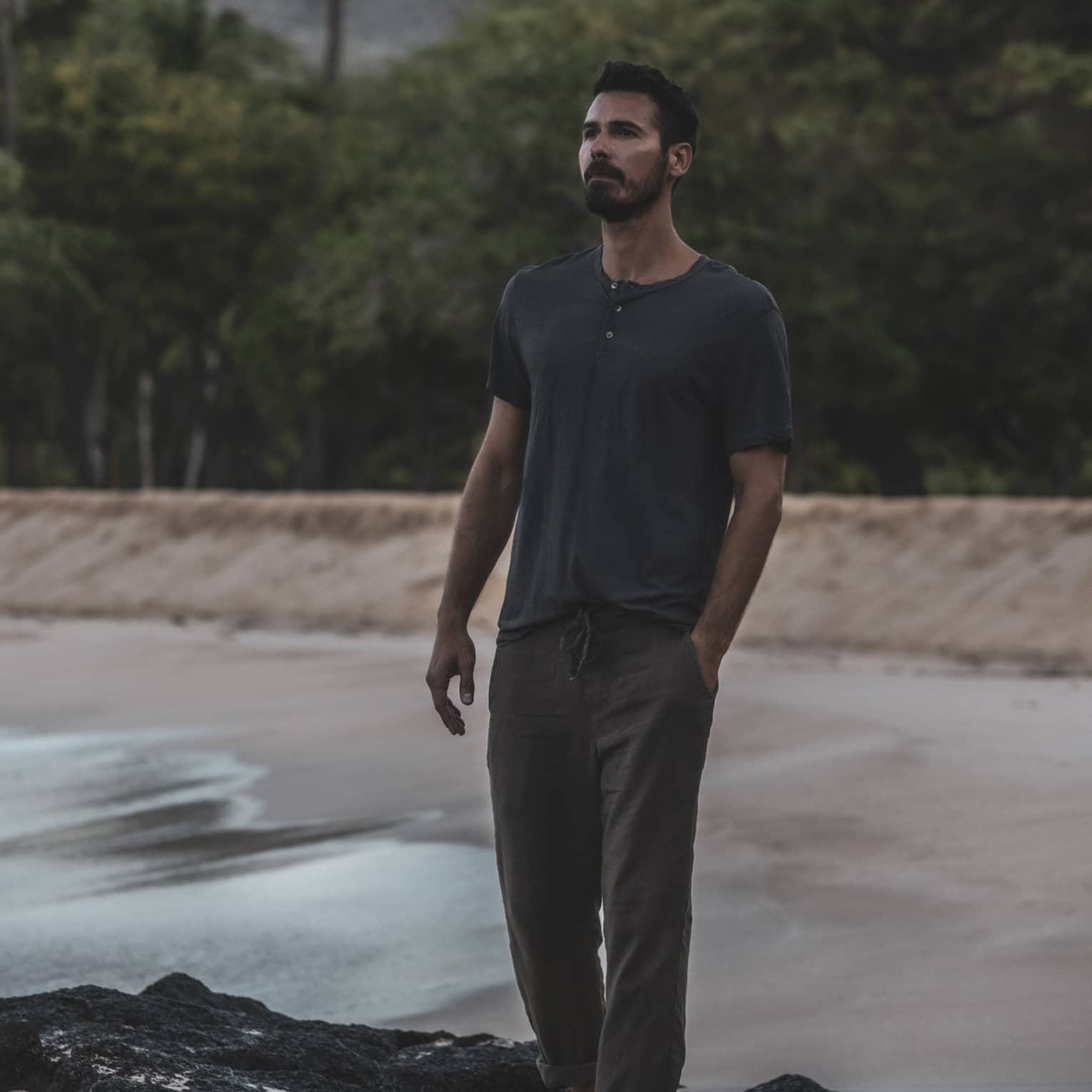 A man walks on a beach in front of a lush tropical forest