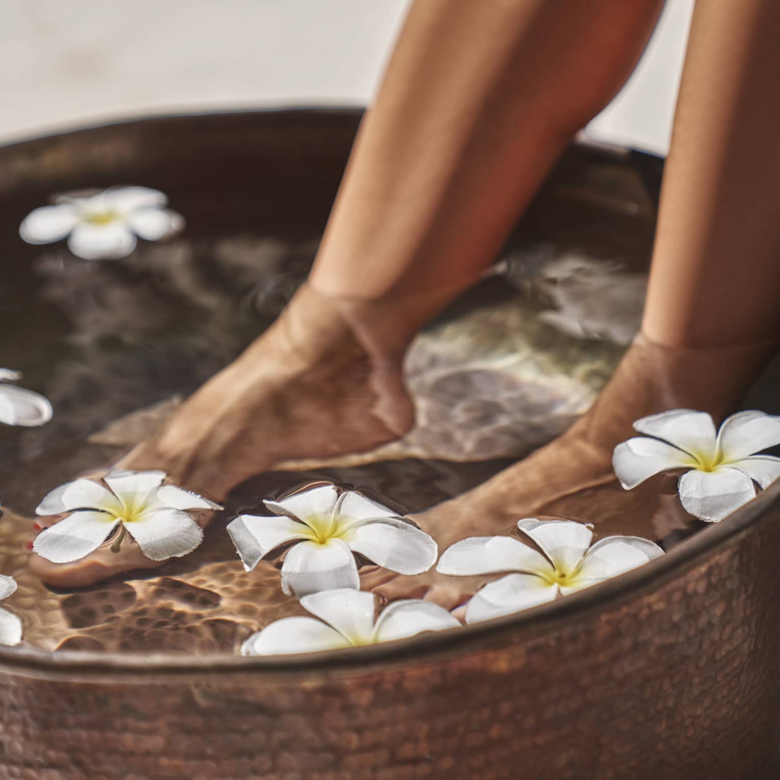 A woman's feet in a bowl of water and flowers.