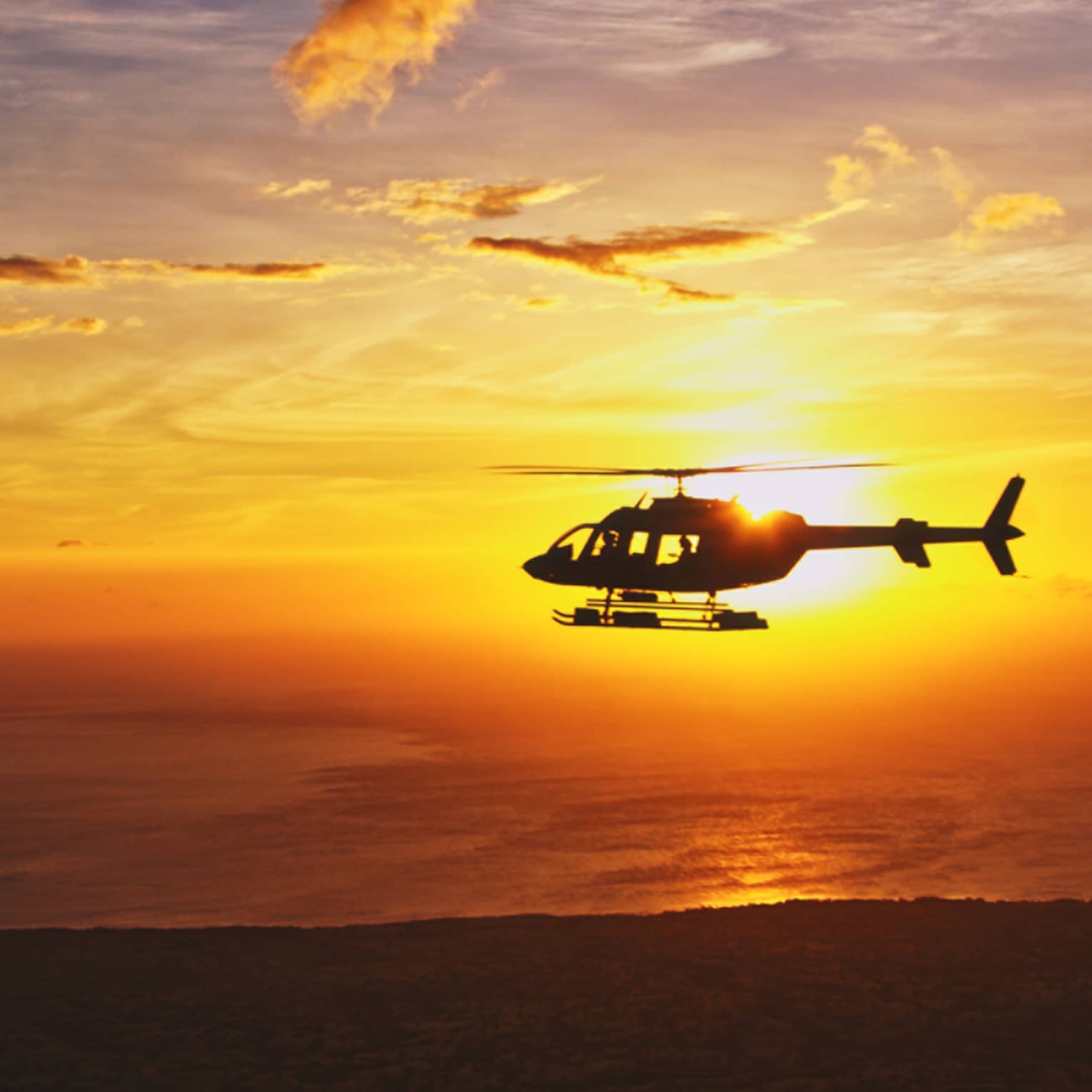 Silhouette of helicopter against orange sunset
