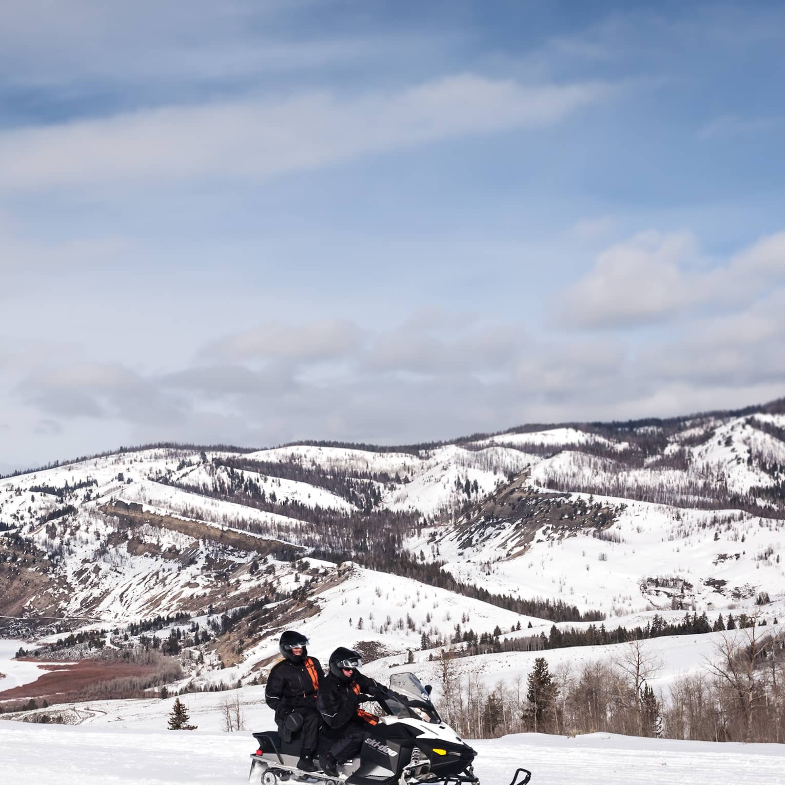 Aerial view of two people riding on a snowmobile in front of snowy mountains