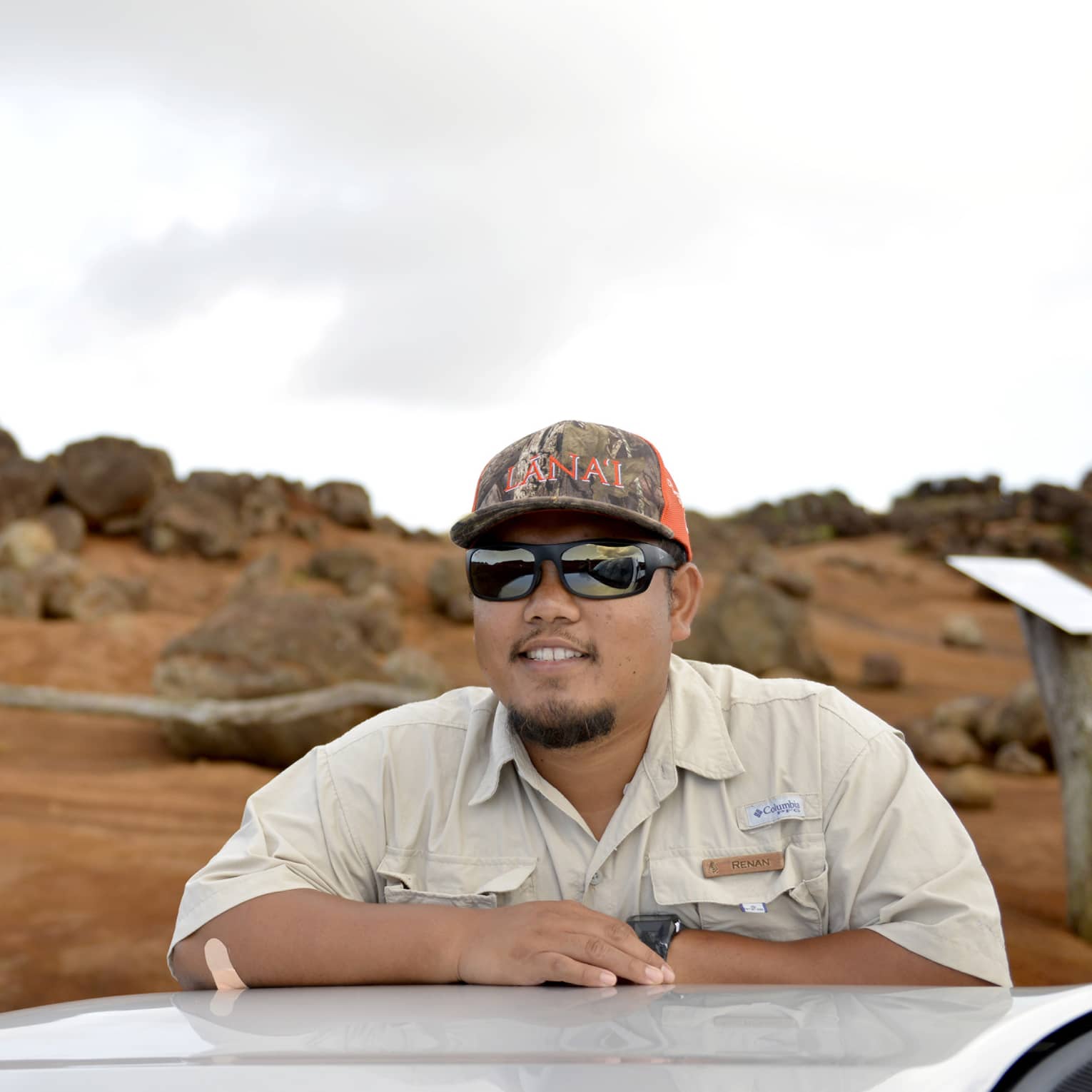 Man leans on top of car, Lanai, Hawaii landscape in the background