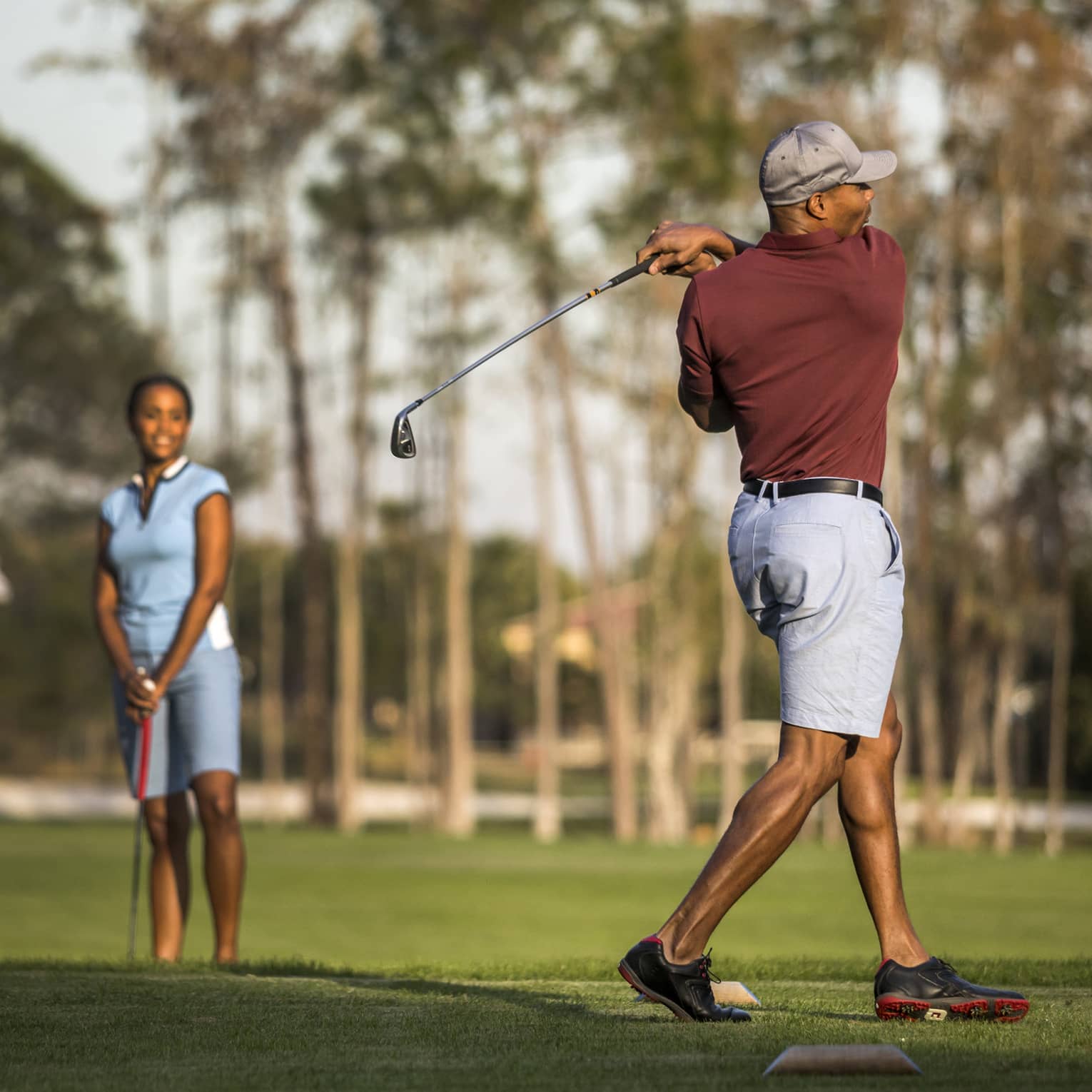Four people standing on a golf course, one person swinging a golf club