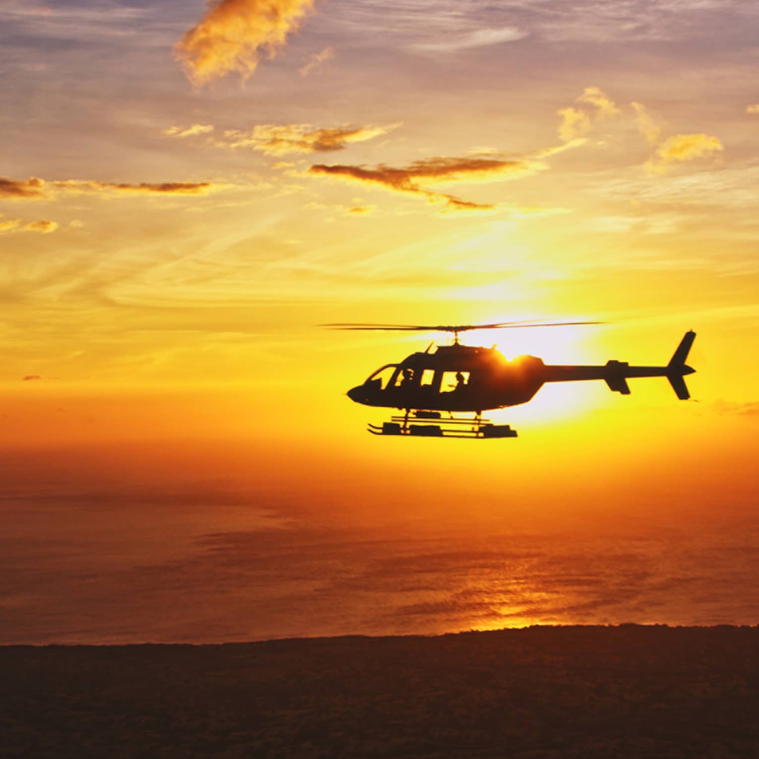 Silhouette of helicopter against orange sunset
