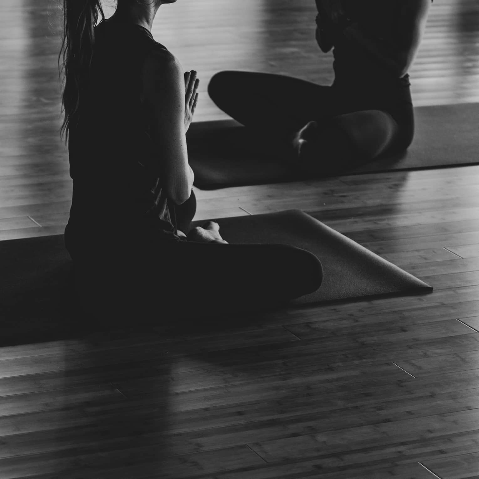 A black and white image of two women practicing yoga in a studio.