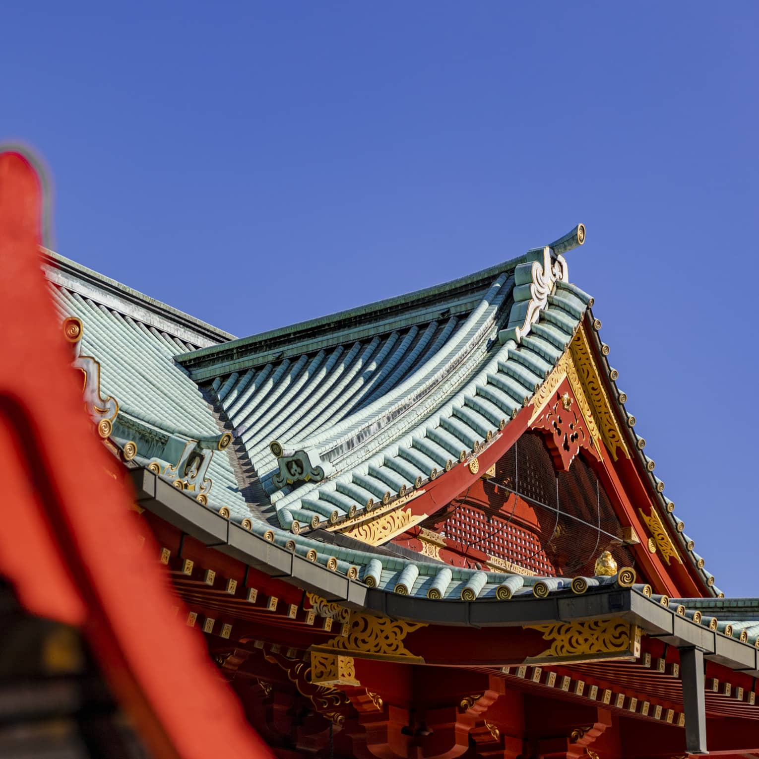 Concave tented gable rooftops of Shinto temples with ornate red and gold facades and grooved piping on the roofs.