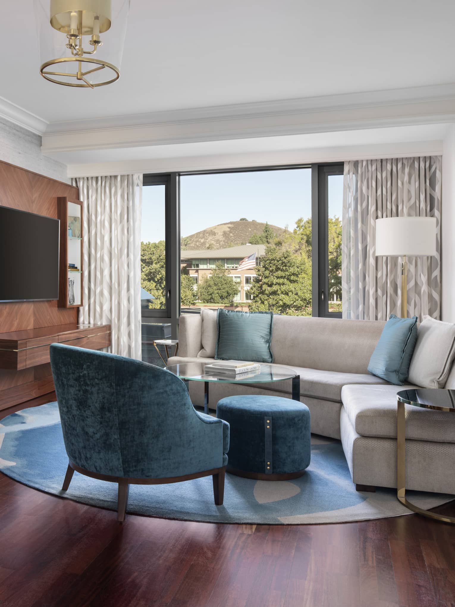Guest room with grey couch with blue pillows, blue lounge chair, round table with two chairs, window view