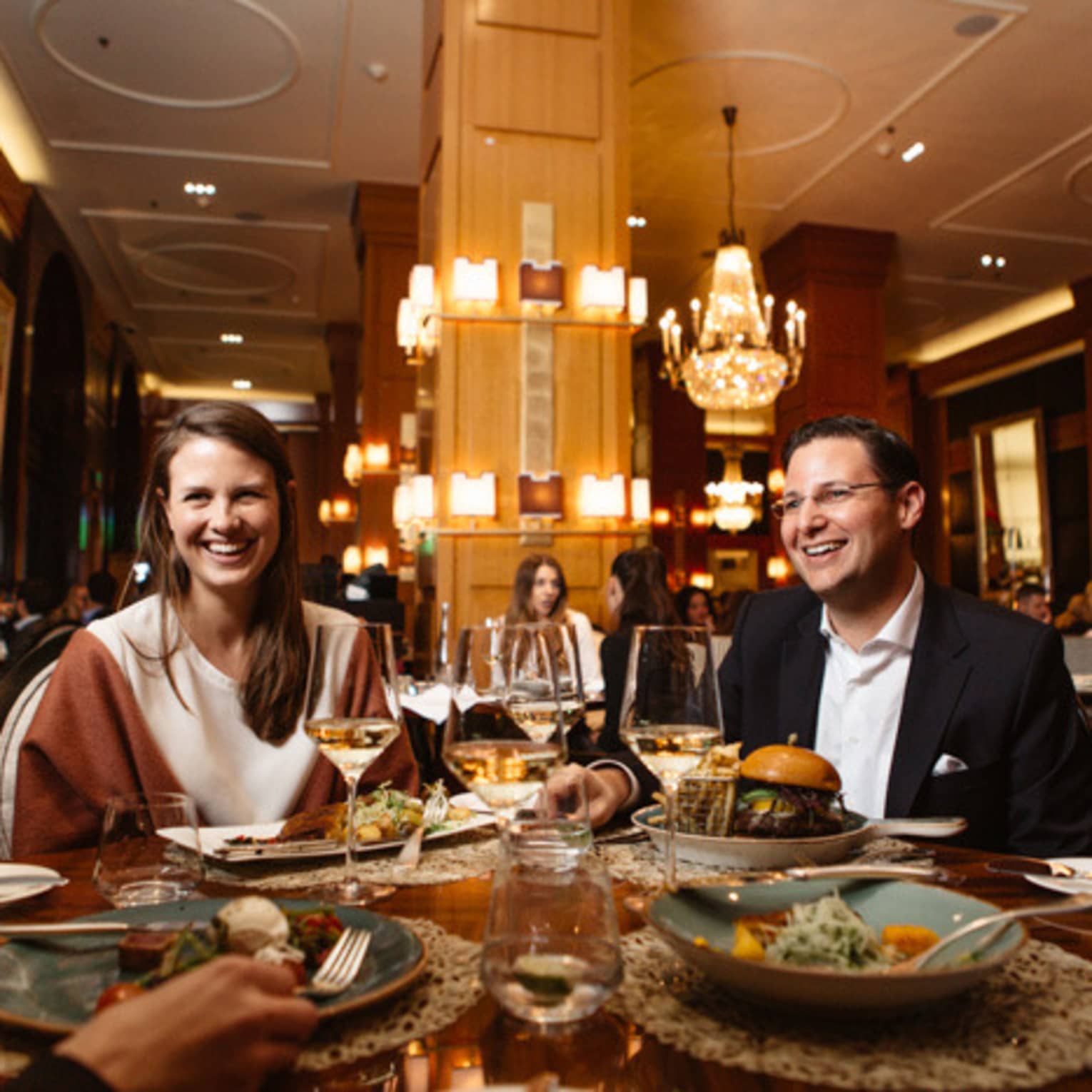 Four people sit around a restaurant table smiling at each other and enjoying a meal