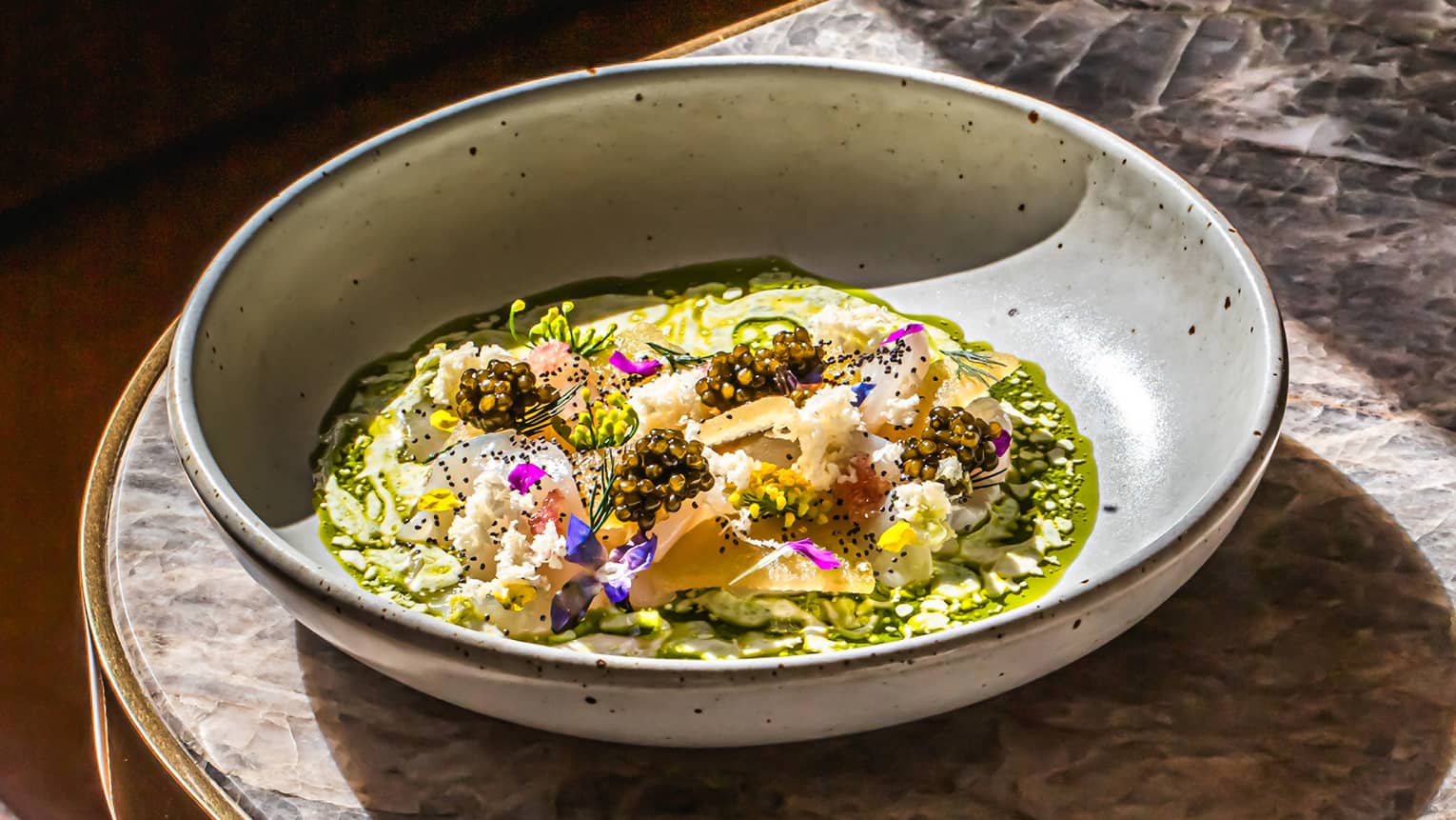 A bowl of colourful food items sits on the corner of a marbled tabletop.