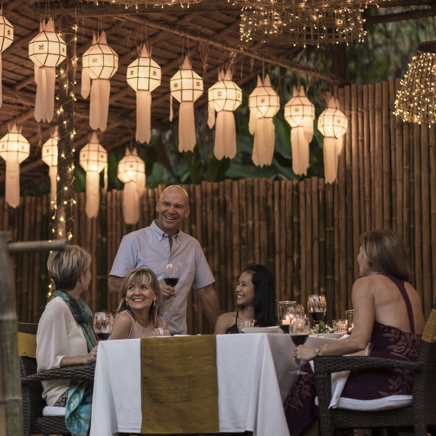 A group of people sitting at a table enjoying a meal in outdoor pavilion decorated with lanterns