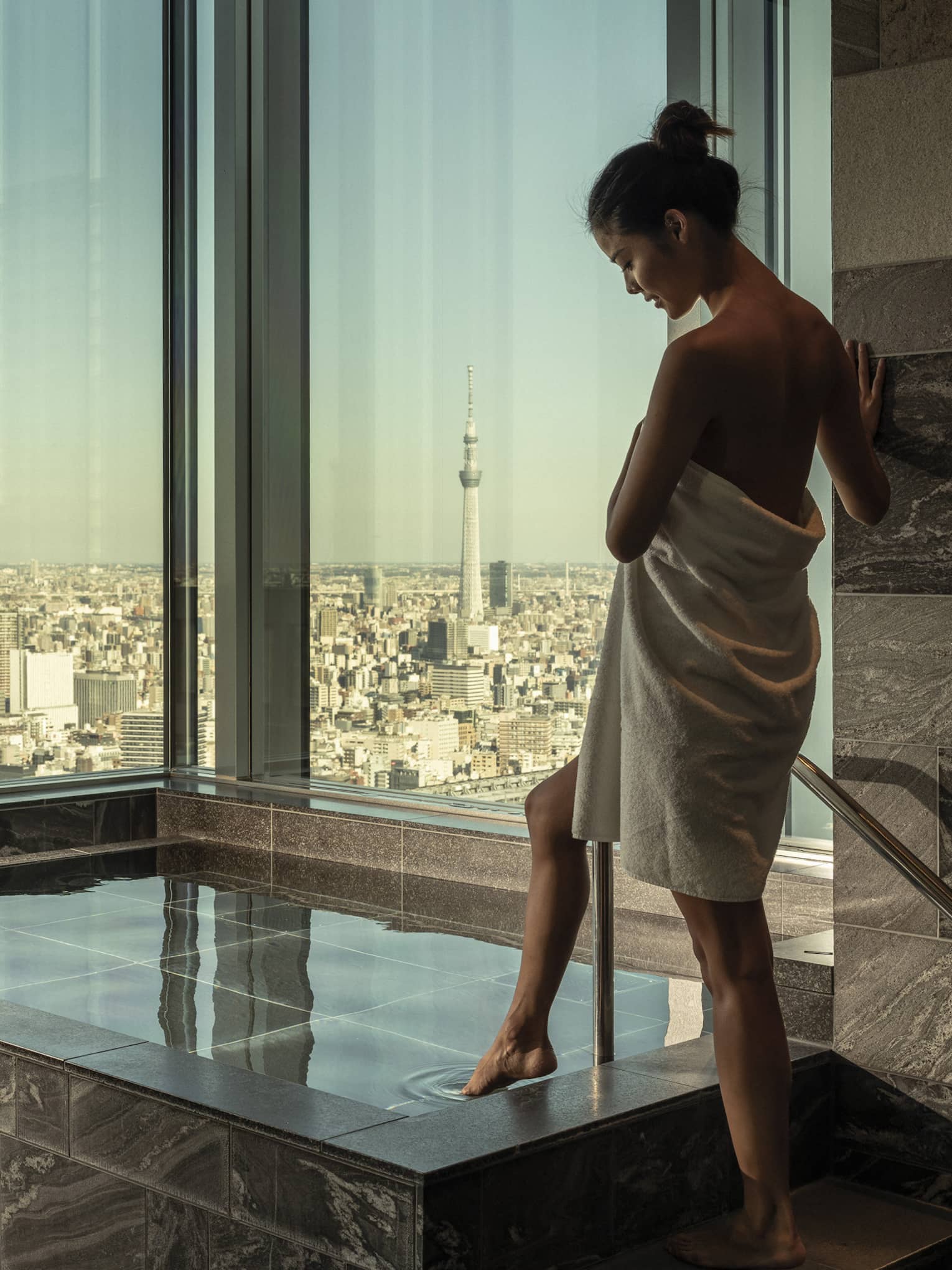 Woman wrapped in white towel dips her toe into the ofuro bath