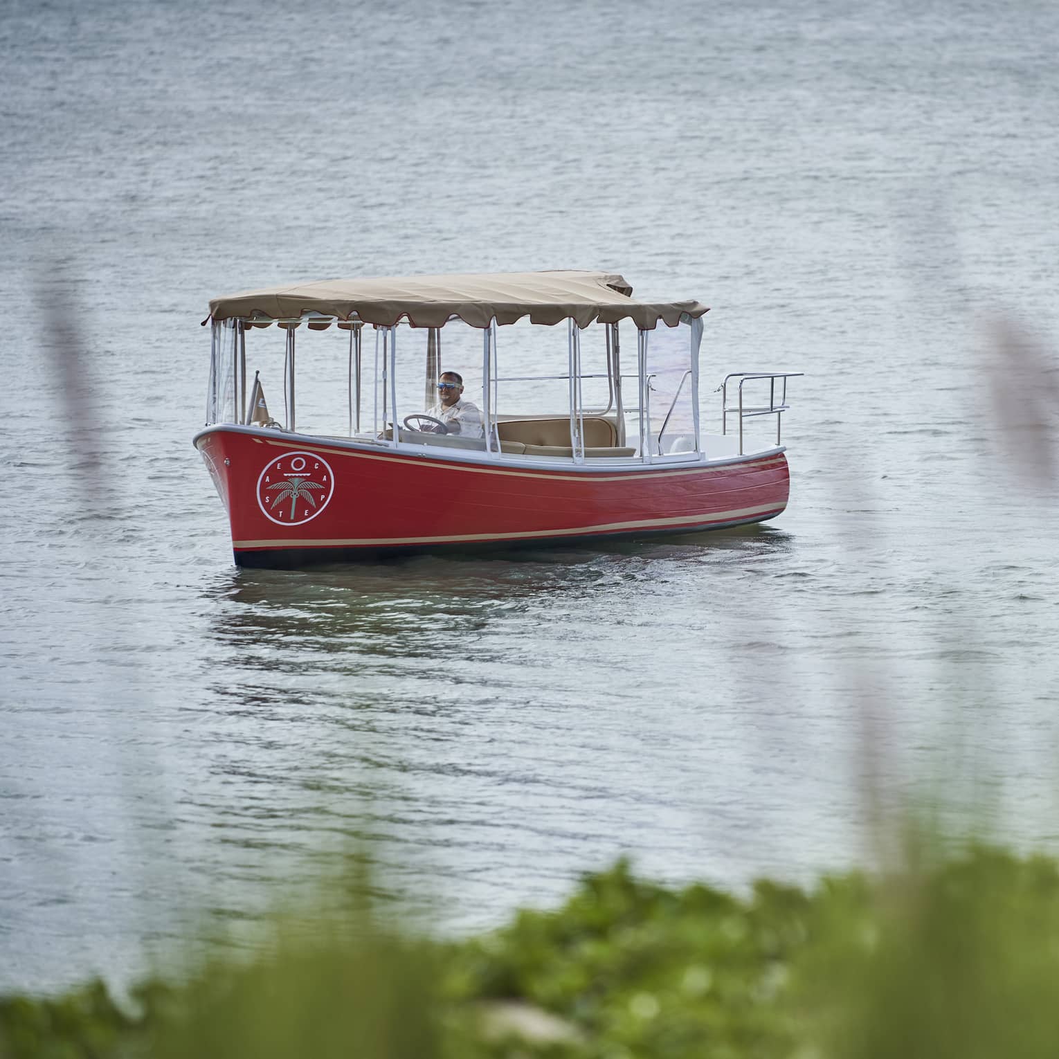 Small red boat with a tan awning floats down a river
