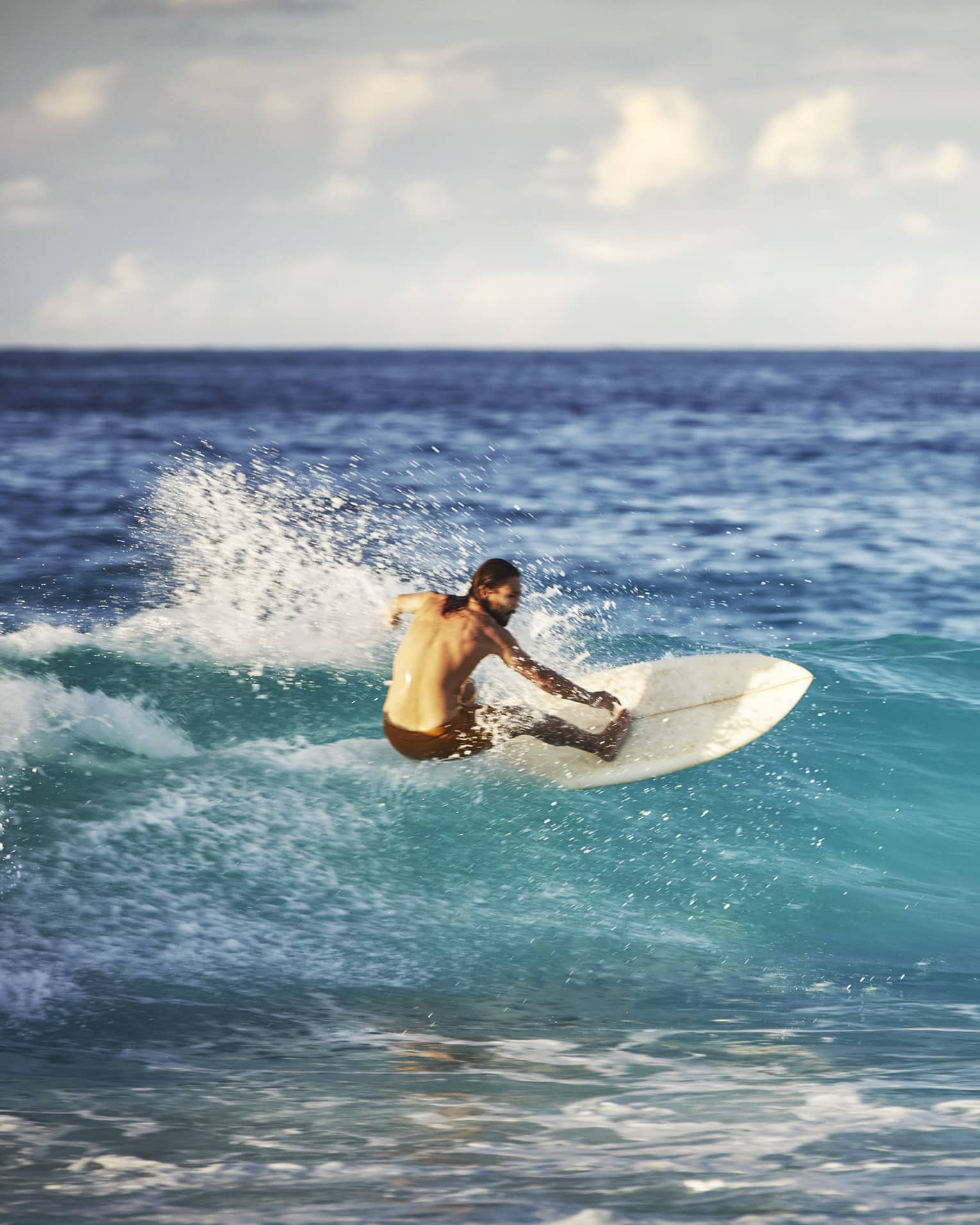 On an expanse of water, a surfer leans back on his board and surfs the face of a wave as white water splashes up behind him.