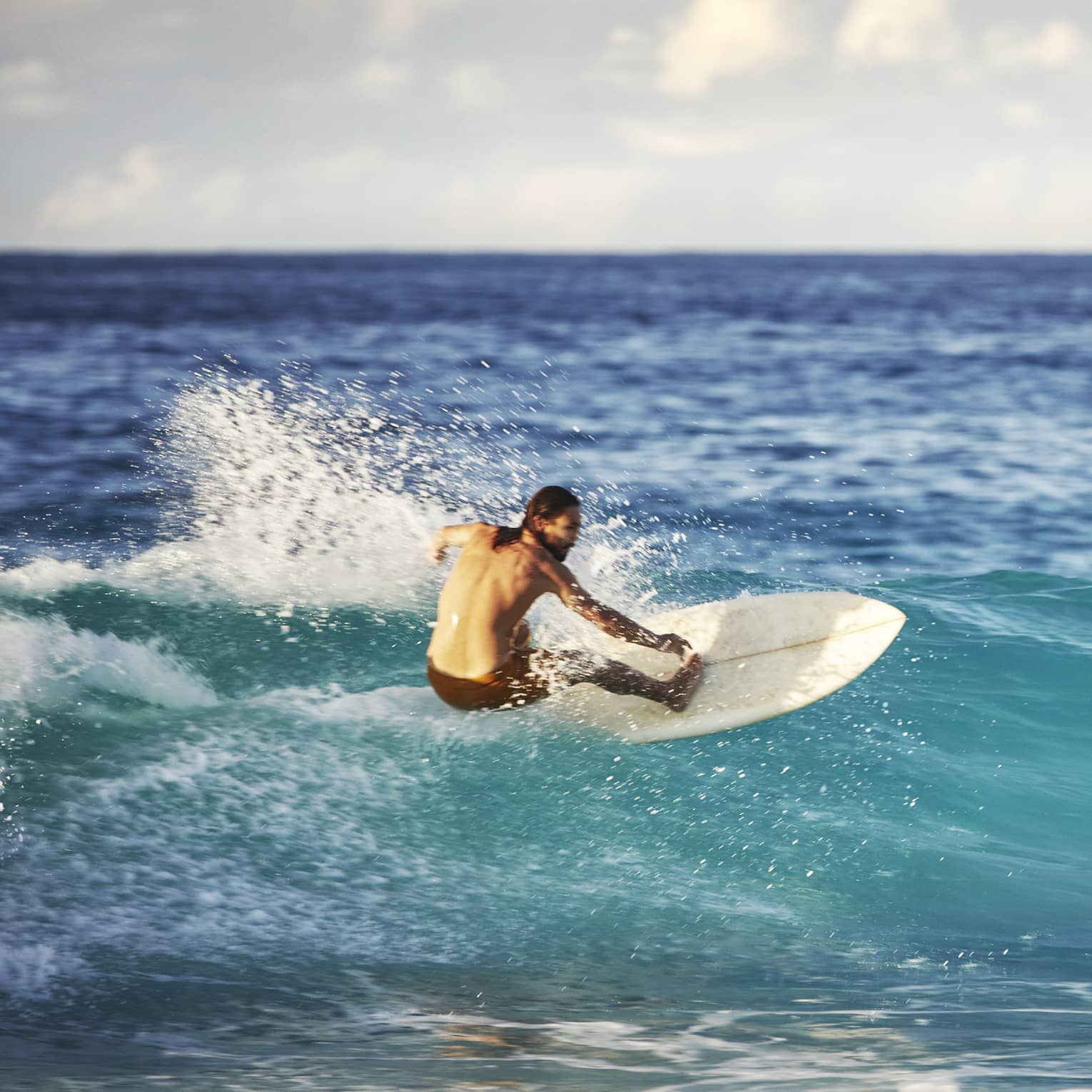 On an expanse of water, a surfer leans back on his board and surfs the face of a wave as white water splashes up behind him.