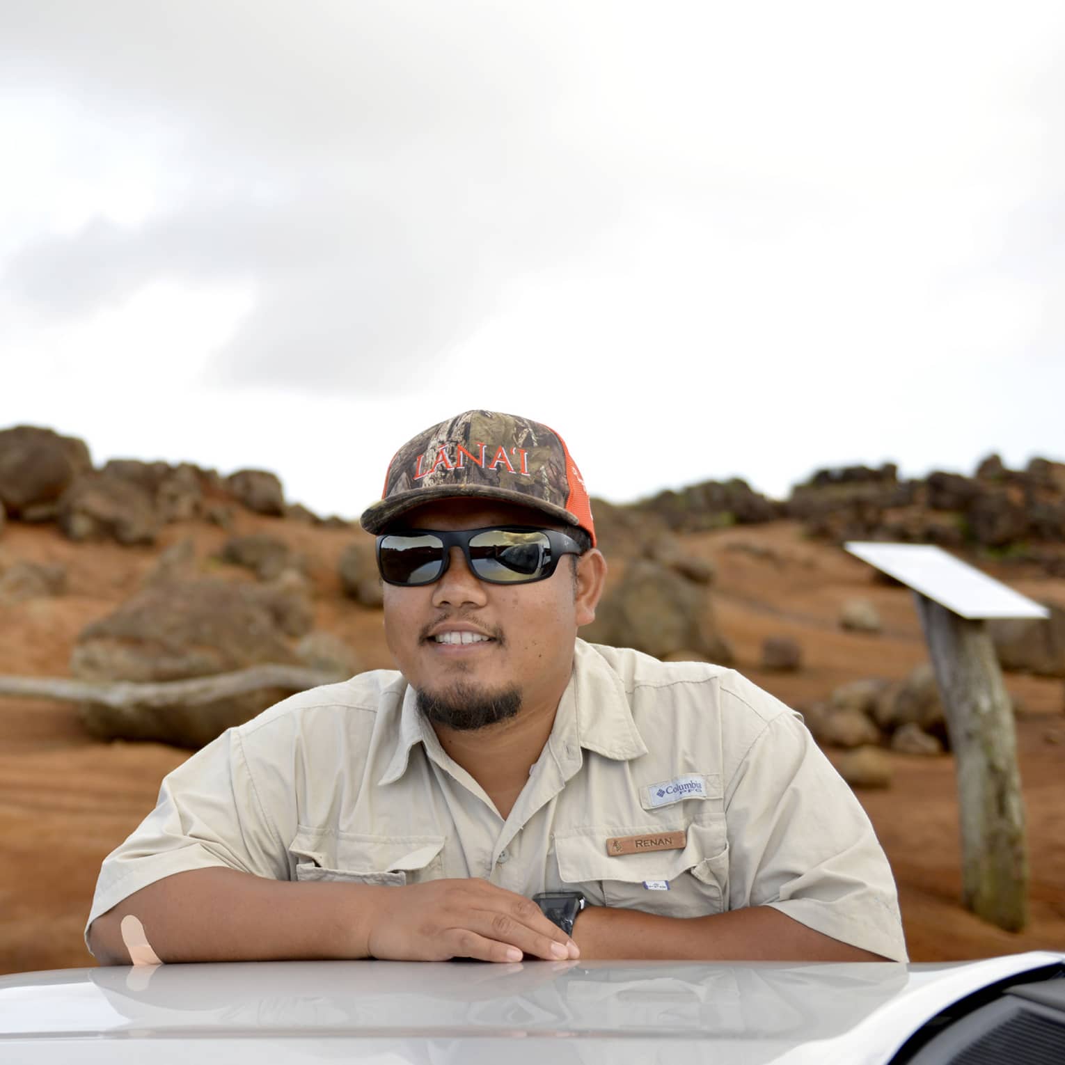 Man leans on top of car, Lanai, Hawaii landscape in the background
