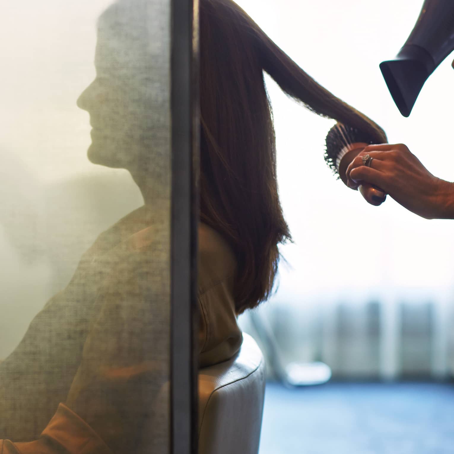 Silhouette of woman behind salon screen as hairdressers brushes, blow dries hair