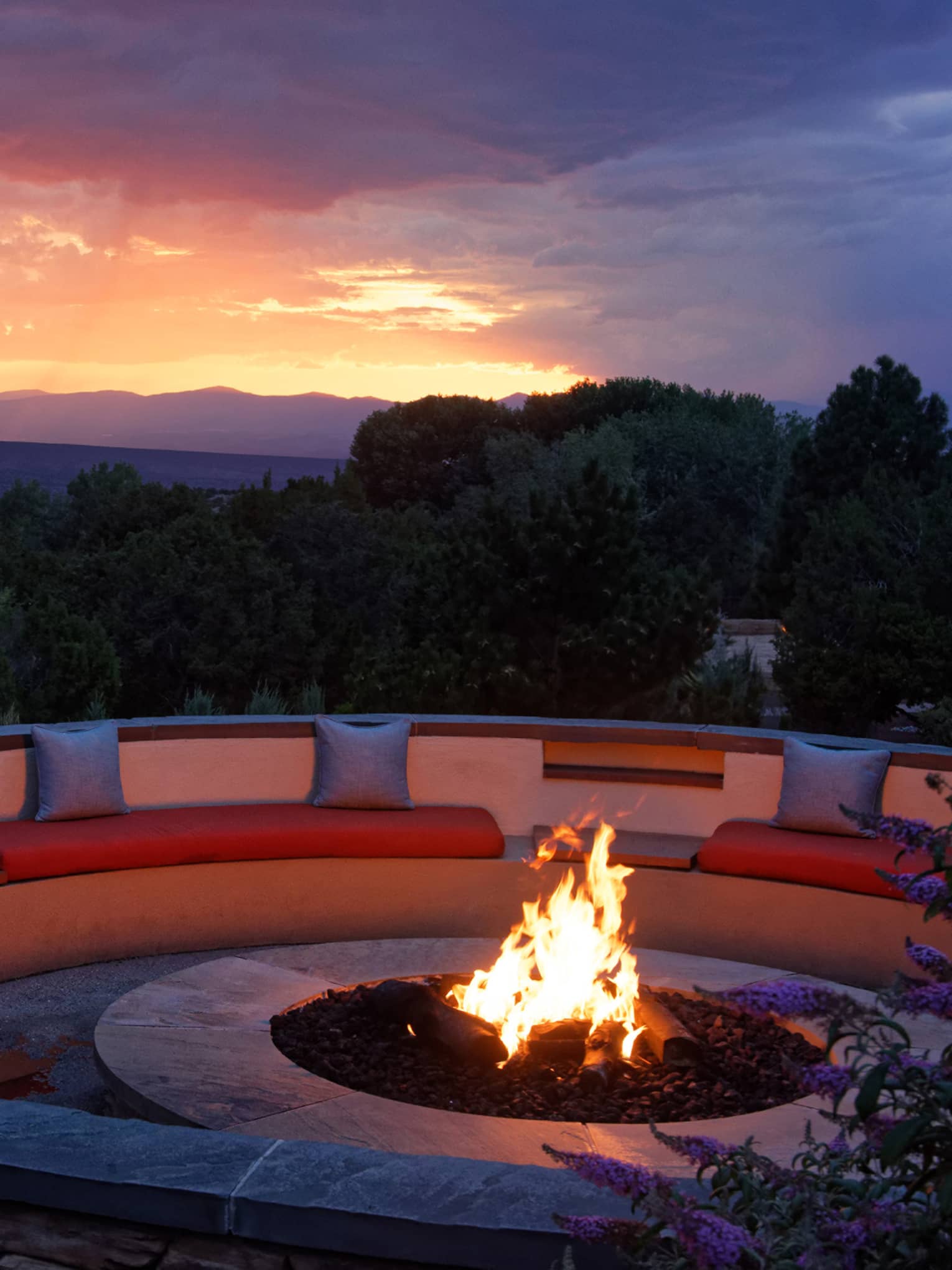 Fire pit with seating surrounding it and a sunset in the background.
