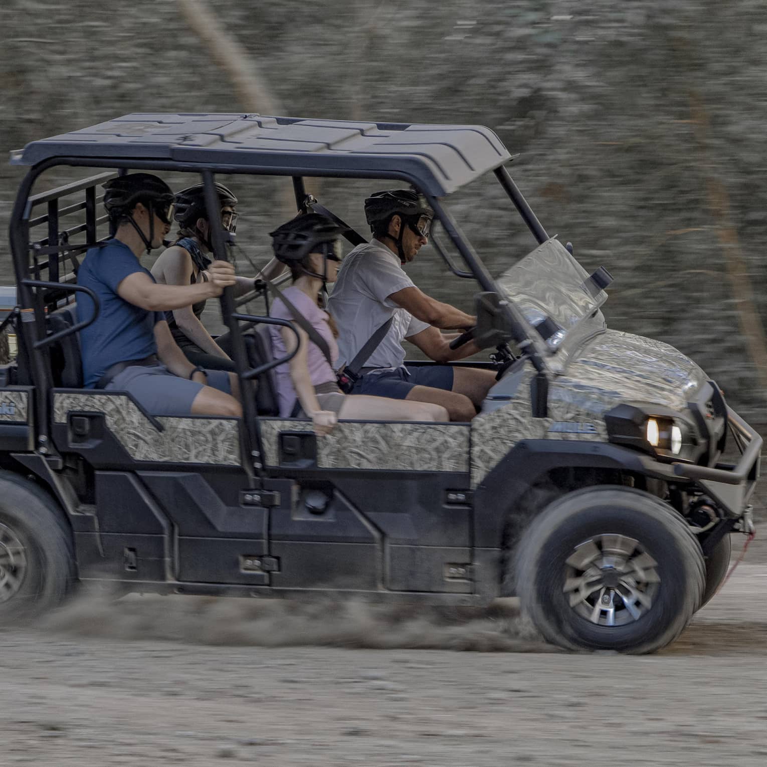 Four people speed along a dirt road in a 4x4 vehicle