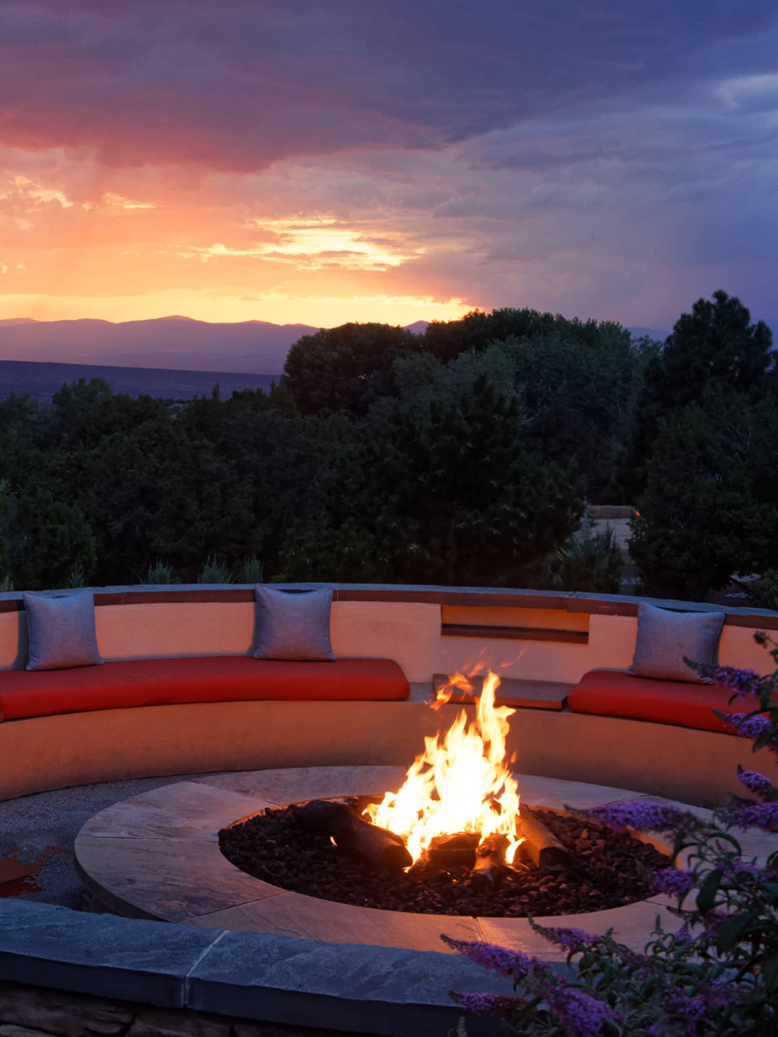 Fire pit with seating surrounding it and a sunset in the background.