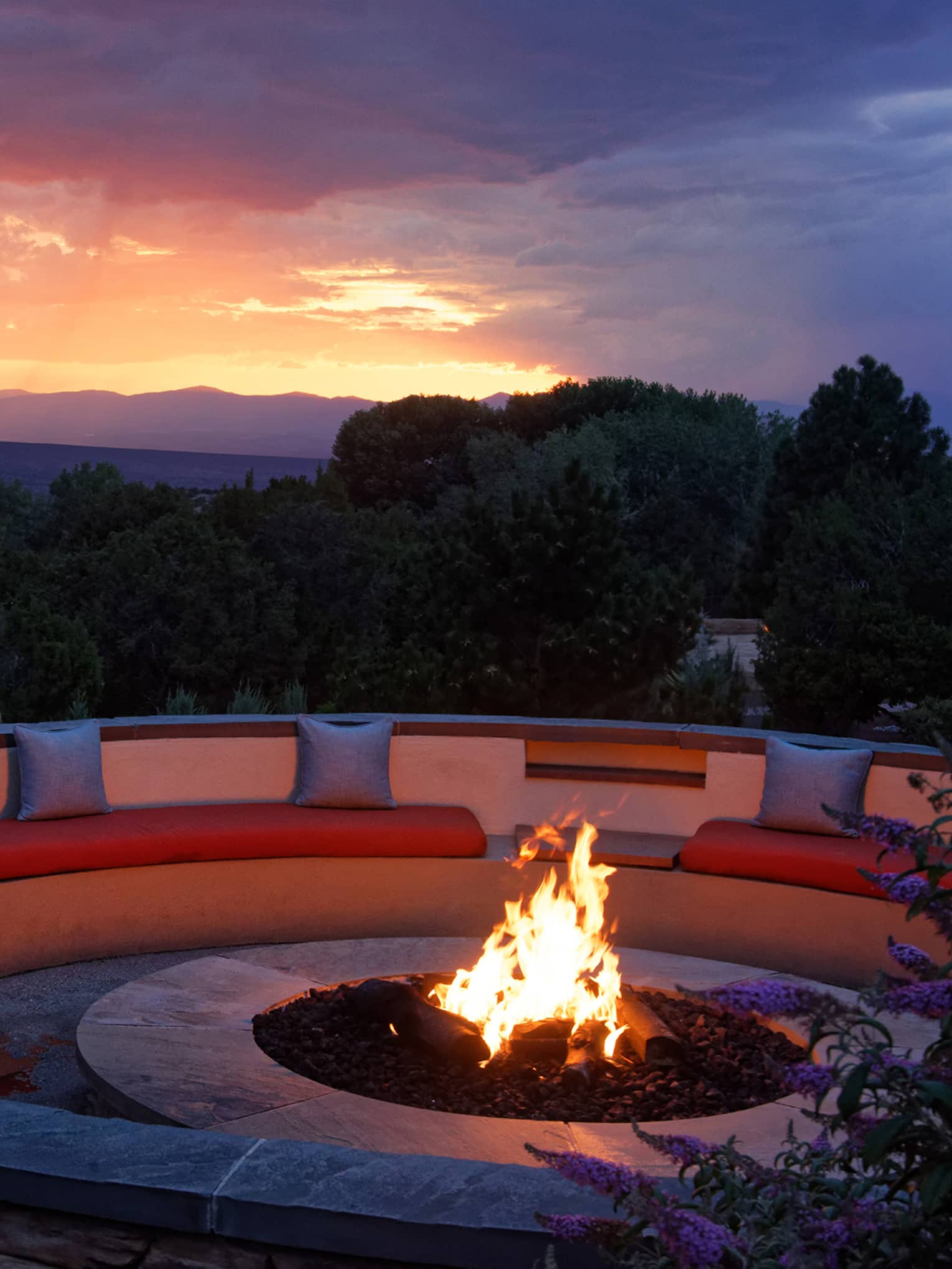 Fire pit with seating surrounding it and a sunset in the background.