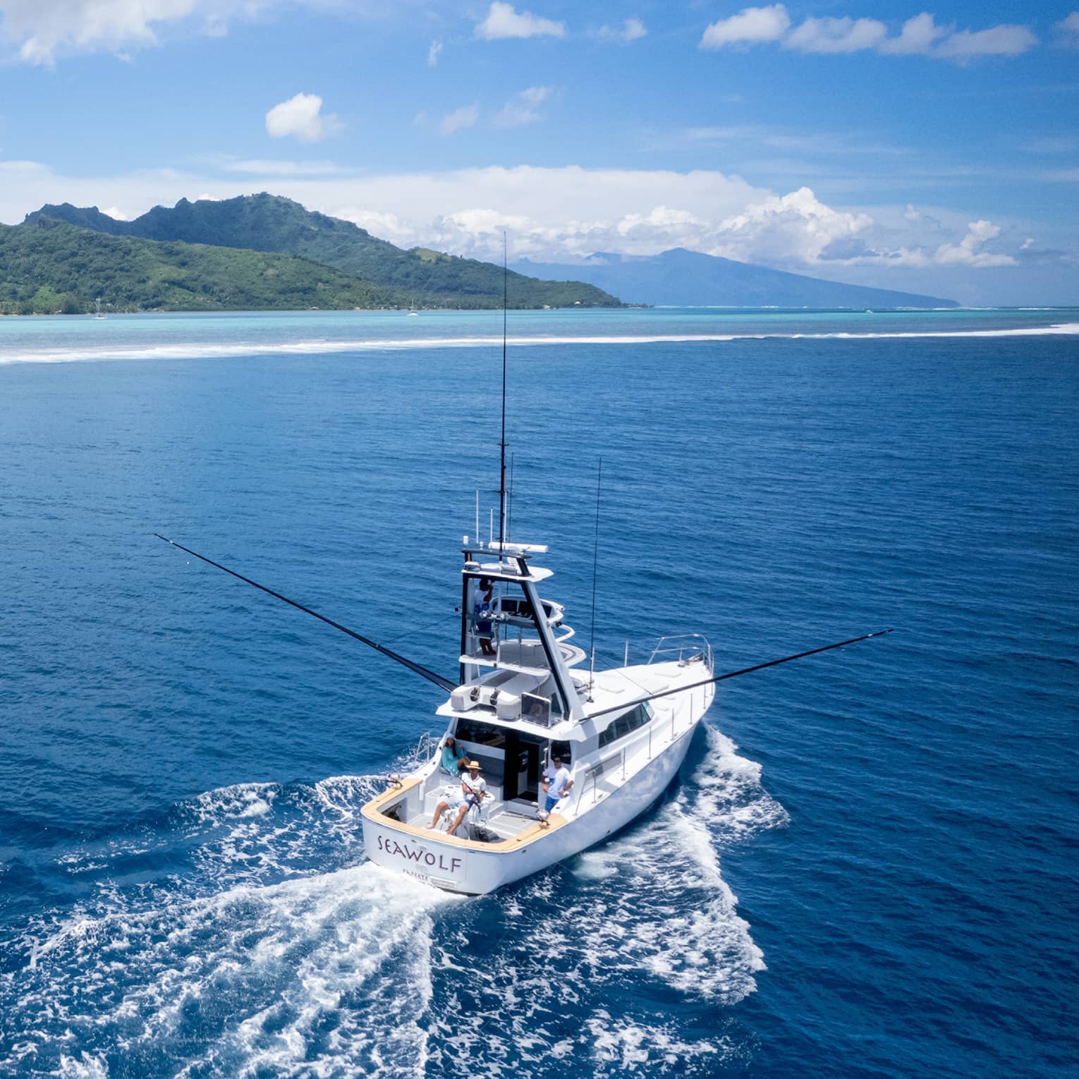 Yacht creates wake in water as it heads out to open sea, lush green mountains in background