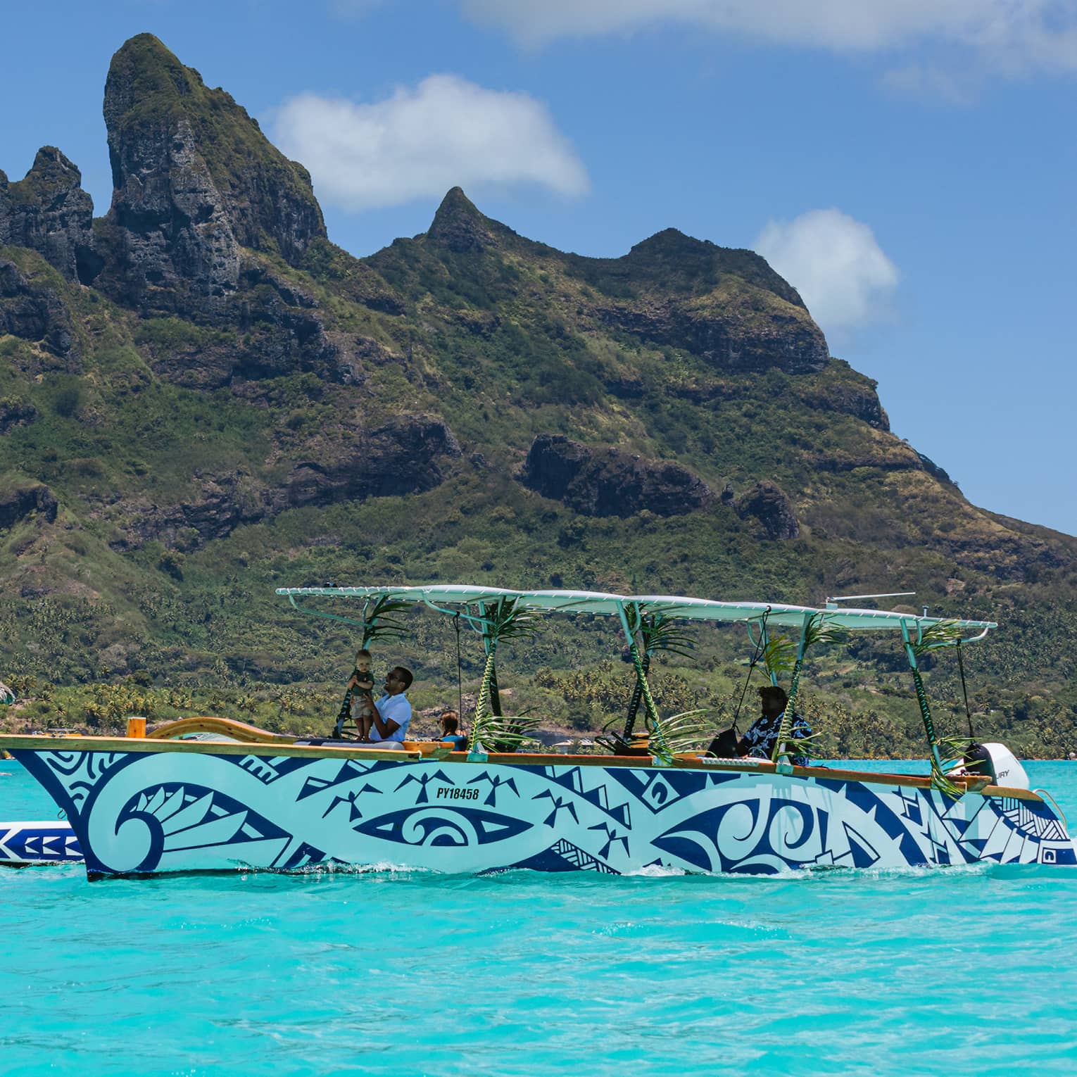 Blue and white patterned boat cruises along turquoise waters with lush green mountains in background